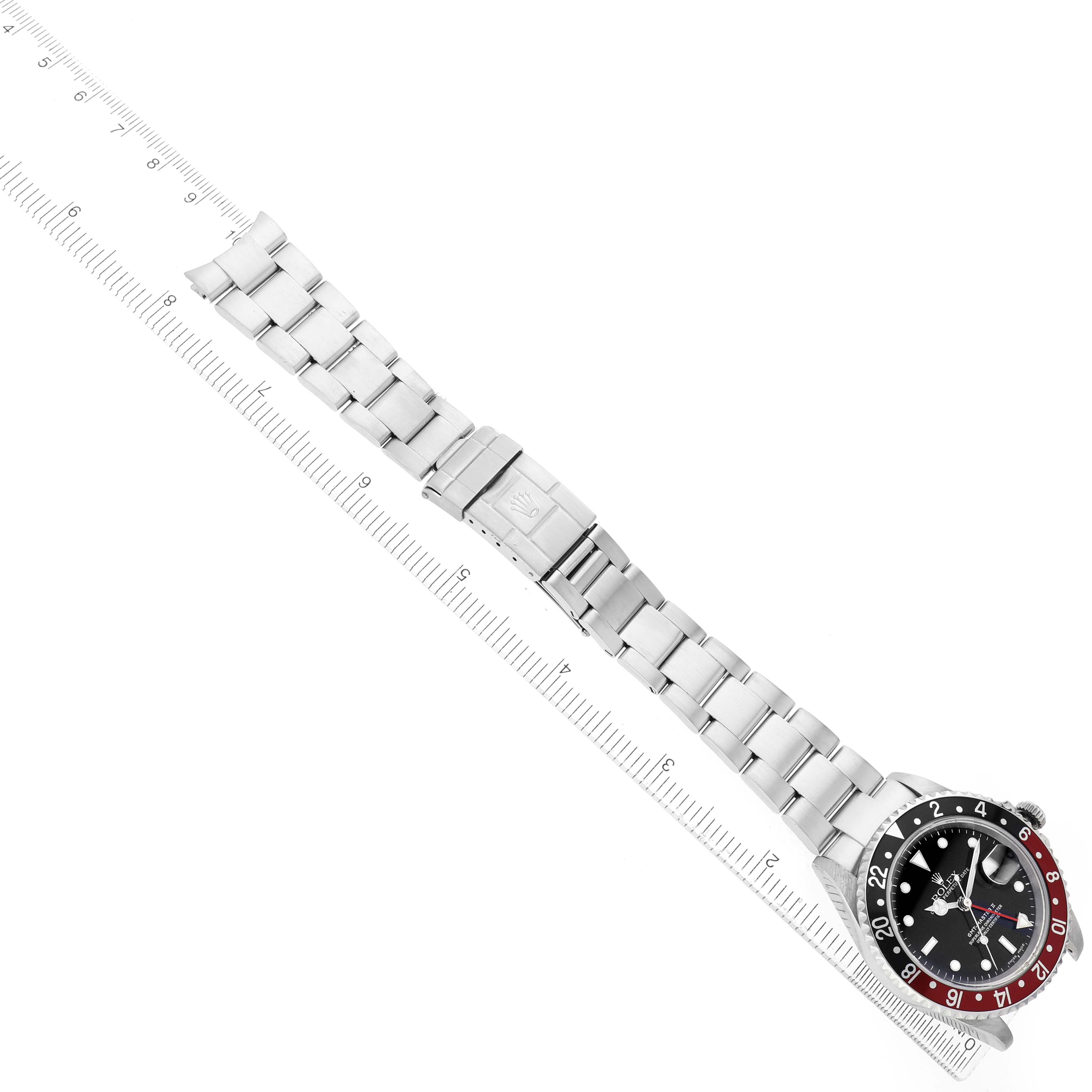 The Rolex GMT-Master 16710 Men's Stainless Steel Black Dial watch is displayed flat, showing the face, bezel, bracelet, and clasp placed diagonally with a ruler beside it.