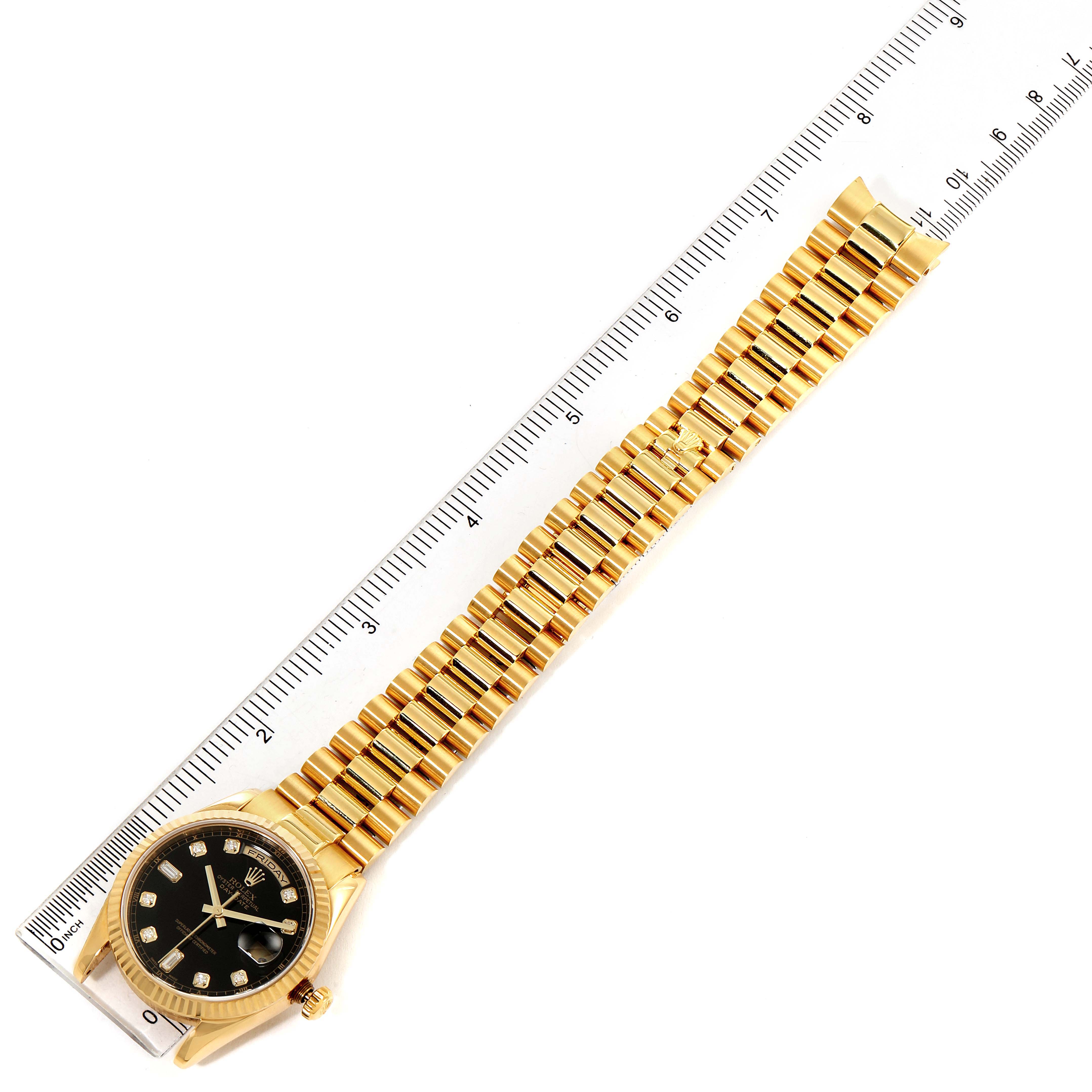 The Rolex President 118238 Men
s Yellow Gold Black Dial 118238 Men
s Yellow Gold Black Dial watch is shown from a top-down angle, displaying the face, bezel, and full gold bracelet next to a ruler.