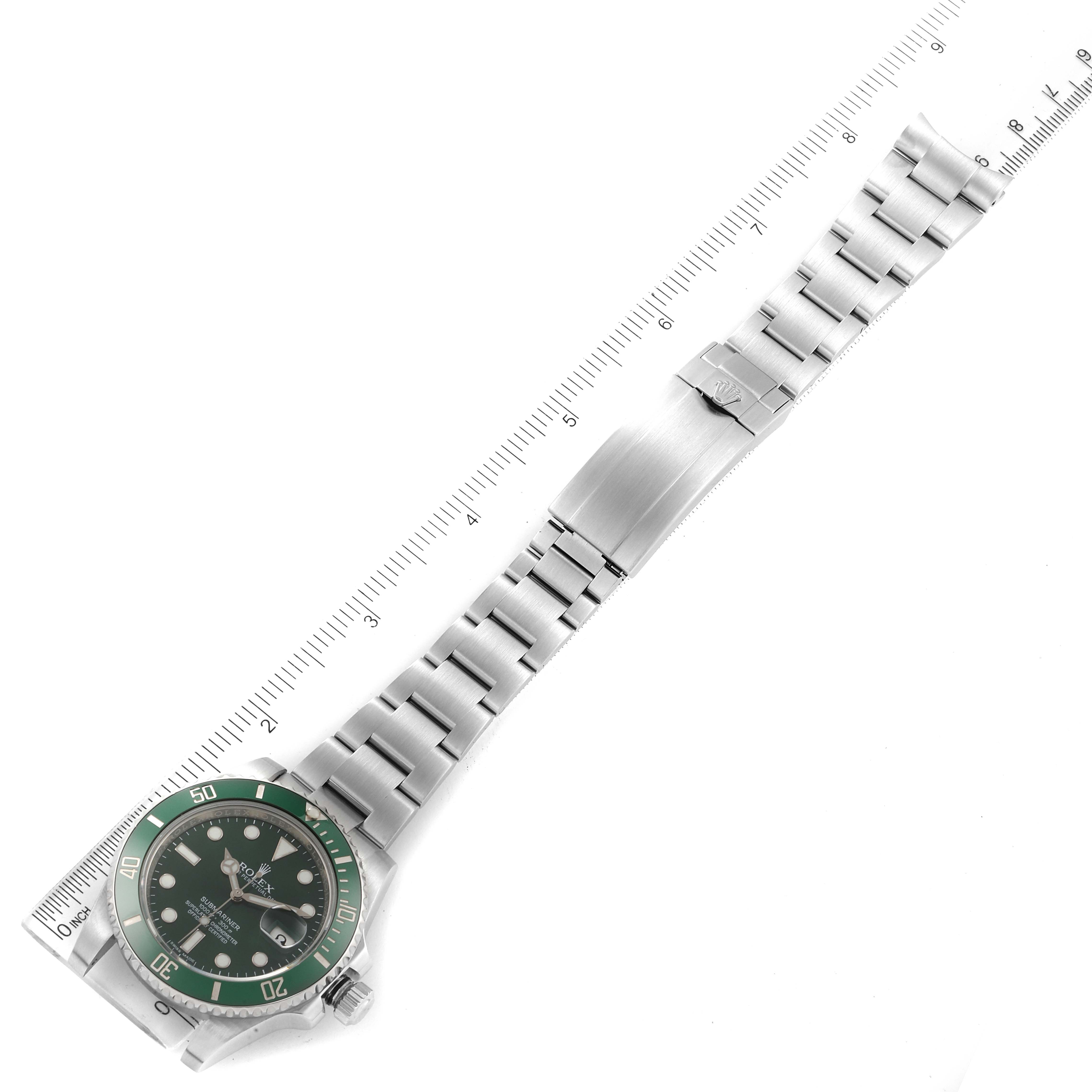 The image shows a Rolex Submariner 116610LV Men
s Stainless Steel Green Dial 116610LV Men
s Stainless Steel Green Dial watch lying flat, showcasing its face, bezel, and stainless steel bracelet alongside a ruler for scale.
