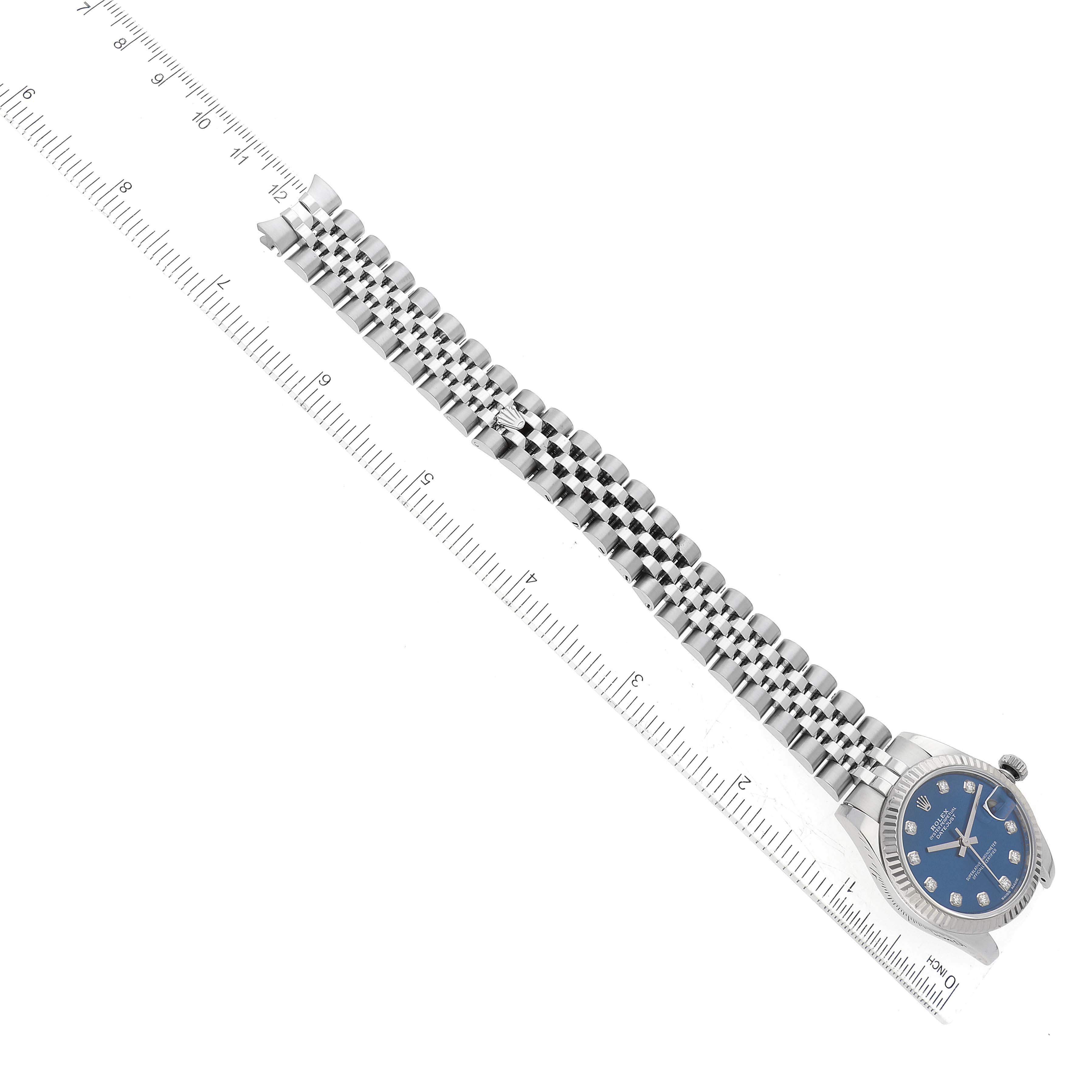 The image shows a top-down view of a Rolex Mid-Size 178274 Women
s Stainless Steel Blue Dial 178274 Women
s Stainless Steel Blue Dial watch, focusing on its face and bracelet, with a ruler placed alongside for scale.