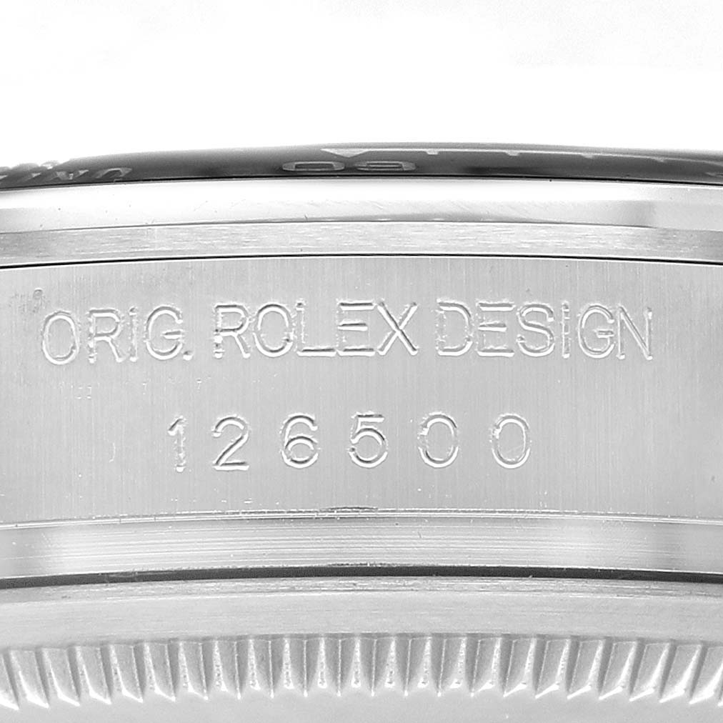 The image shows a close-up of the side of a Rolex Daytona 126500 Men's Stainless Steel White Dial, displaying its engraved model number and "ORIG. ROLEX DESIGN" text.