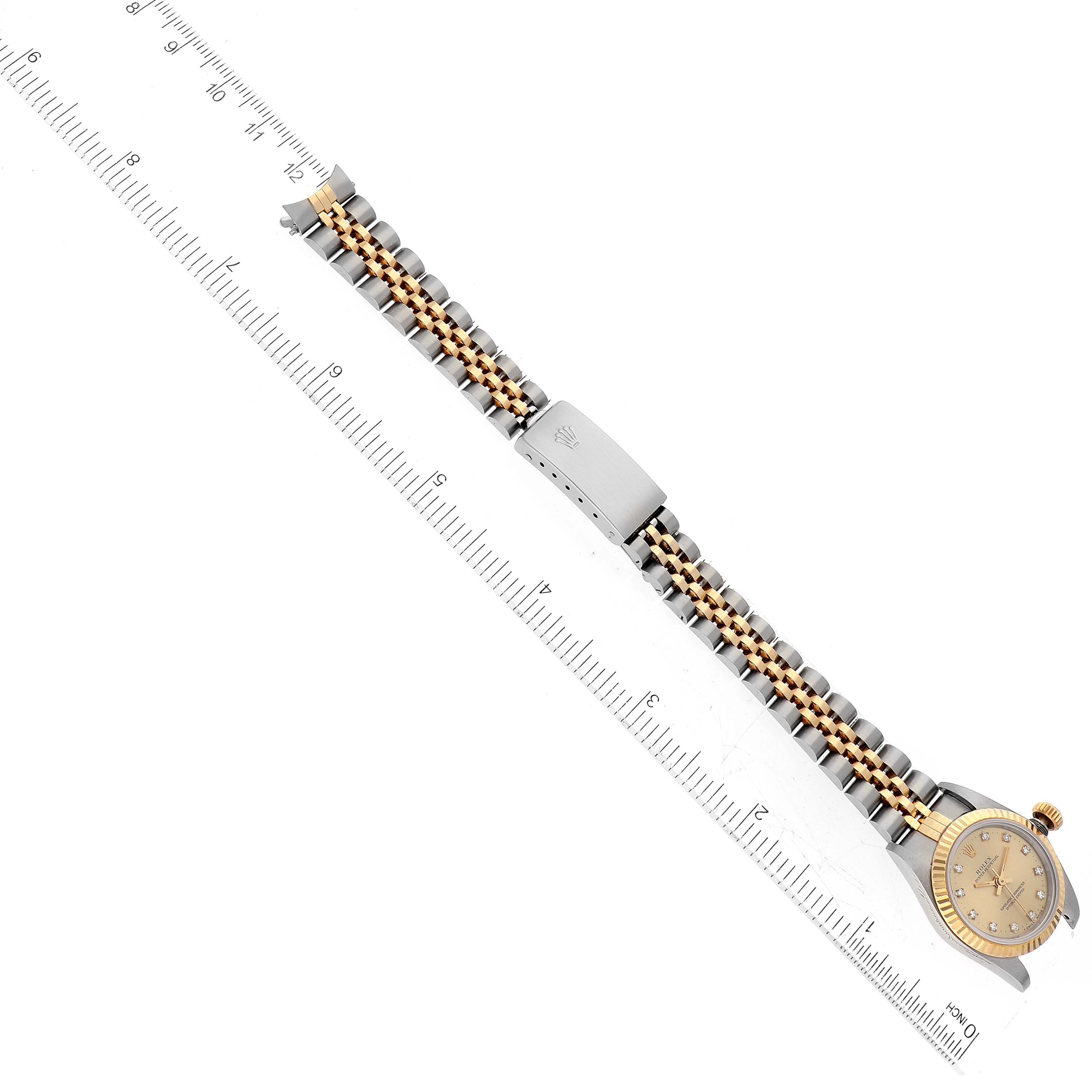 This image shows the side of a Rolex Oyster Perpetual M67193 Women's Steel and Gold (two tone) Champagne Dial M67193 Women's Steel and Gold (two tone) Champagne Dial watch with its two-tone metal bracelet fully extended next to a ruler for size reference.