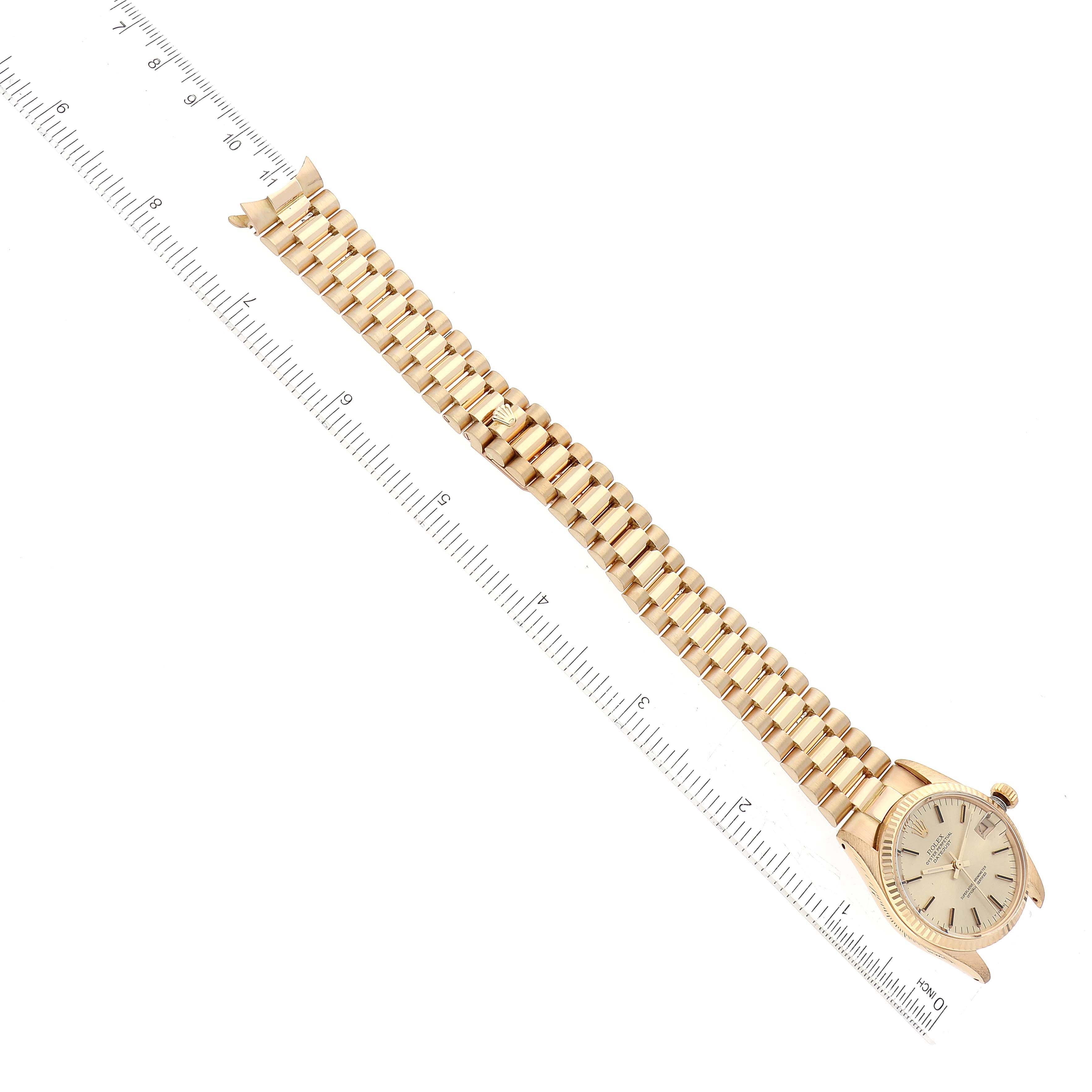 This image shows a top view of a Rolex President M6827/8 Women's Yellow Gold Champagne Dial M6827/8 Women's Yellow Gold Champagne Dial model watch with its gold bracelet extended and a ruler beside it for scale.