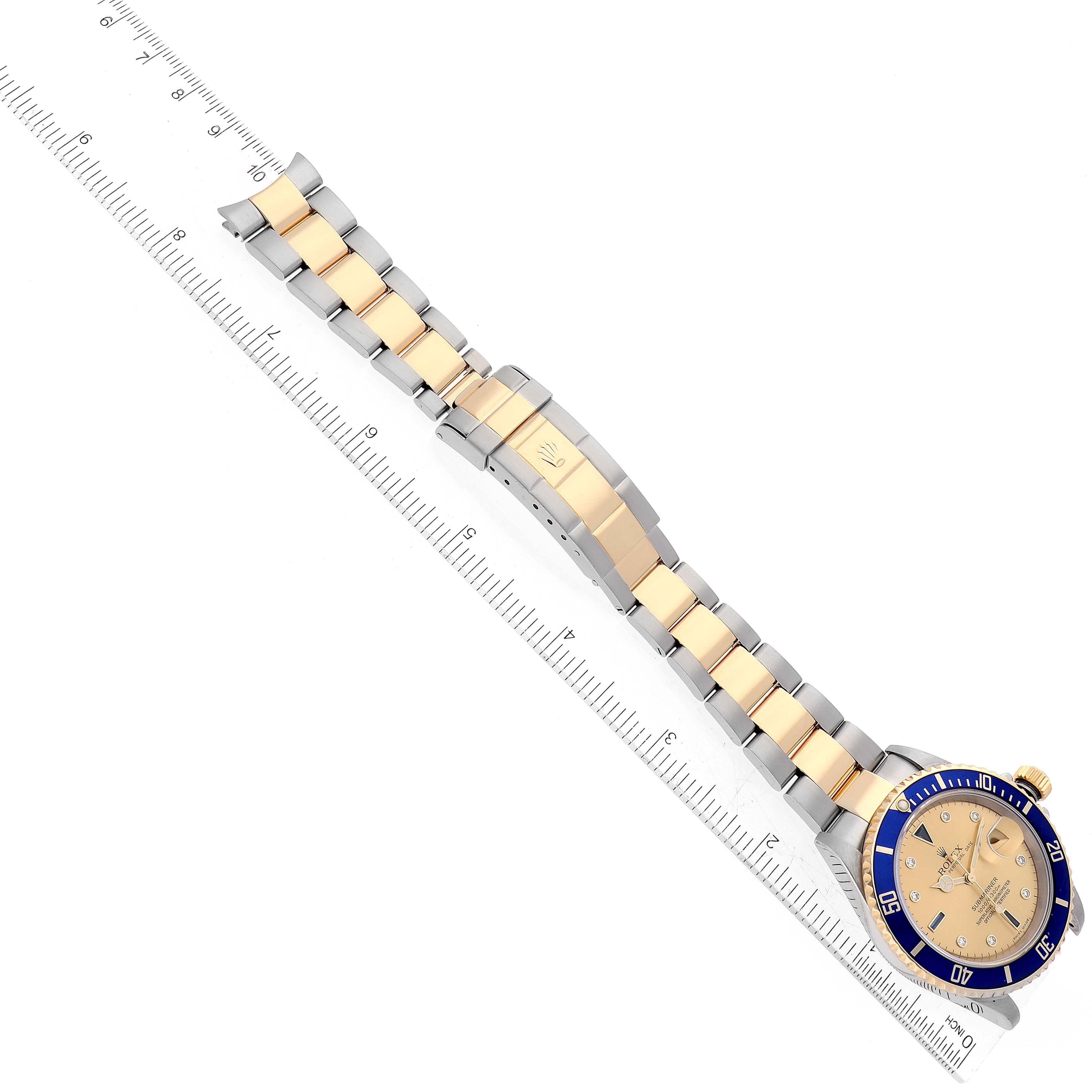 The image shows a Rolex Submariner 16613 Men's Steel and Gold (two tone) Champagne Dial 16613 Men's Steel and Gold (two tone) Champagne Dial watch viewed from above, with its band extended alongside a ruler.