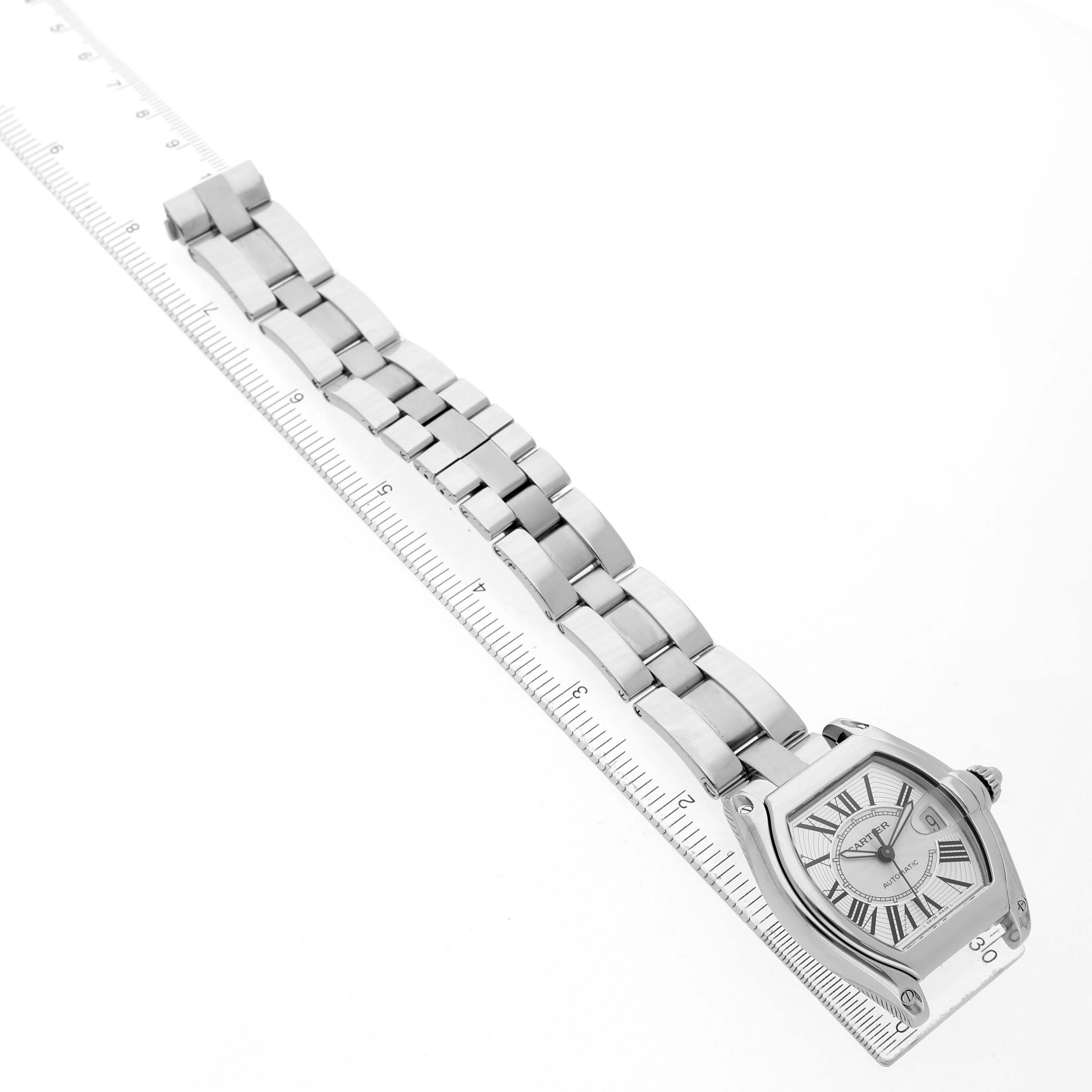 The Cartier Roadster W62025V3 Men's Stainless Steel Silver Dial watch is displayed diagonally, showcasing its face and full metal bracelet alongside a measuring ruler.