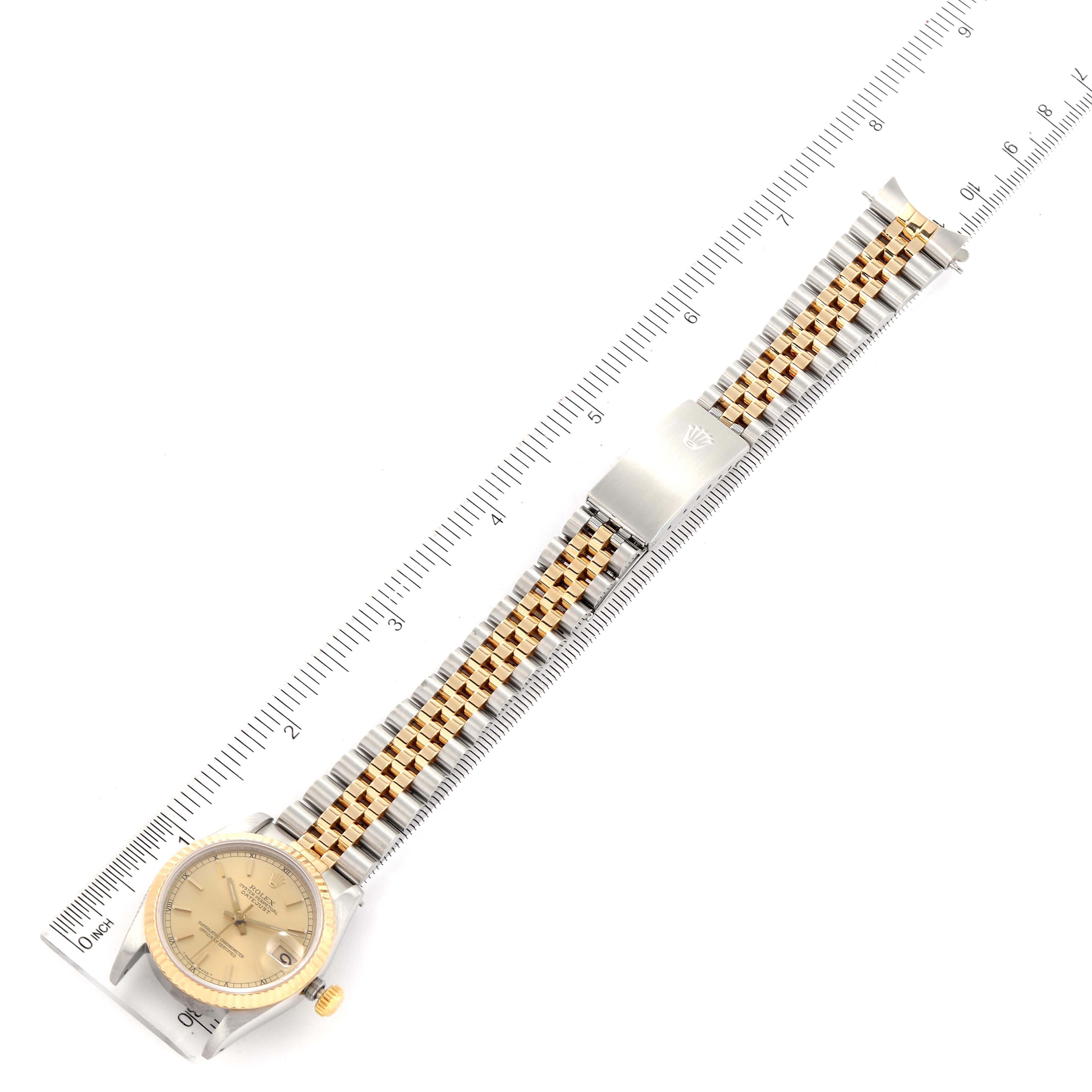 The image shows a top-down view of a Rolex Mid-Size 68273 Women
s Steel and Gold (two tone) Champagne Dial 68273 Women
s Steel and Gold (two tone) Champagne Dial watch, featuring its face, bezel, crown, and bracelet against a ruler for scale.