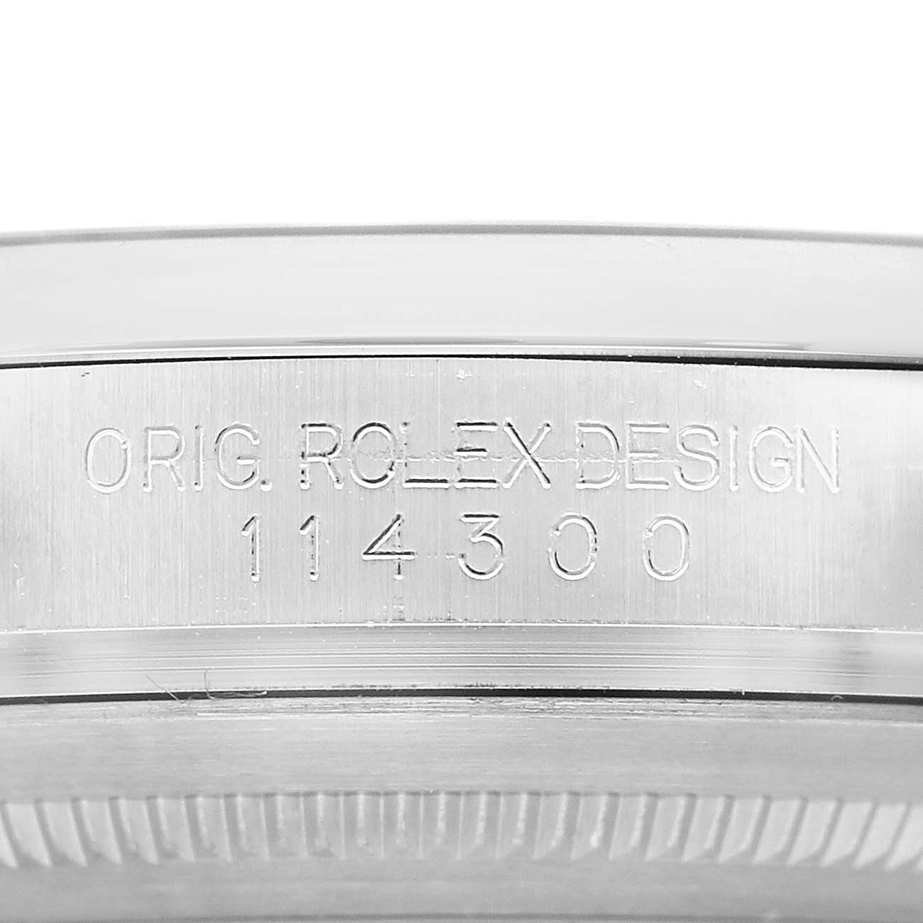 The image shows the side of a Rolex Oyster Perpetual 114300 Men's Stainless Steel Blue Dial watch, highlighting the engraved design and model number.