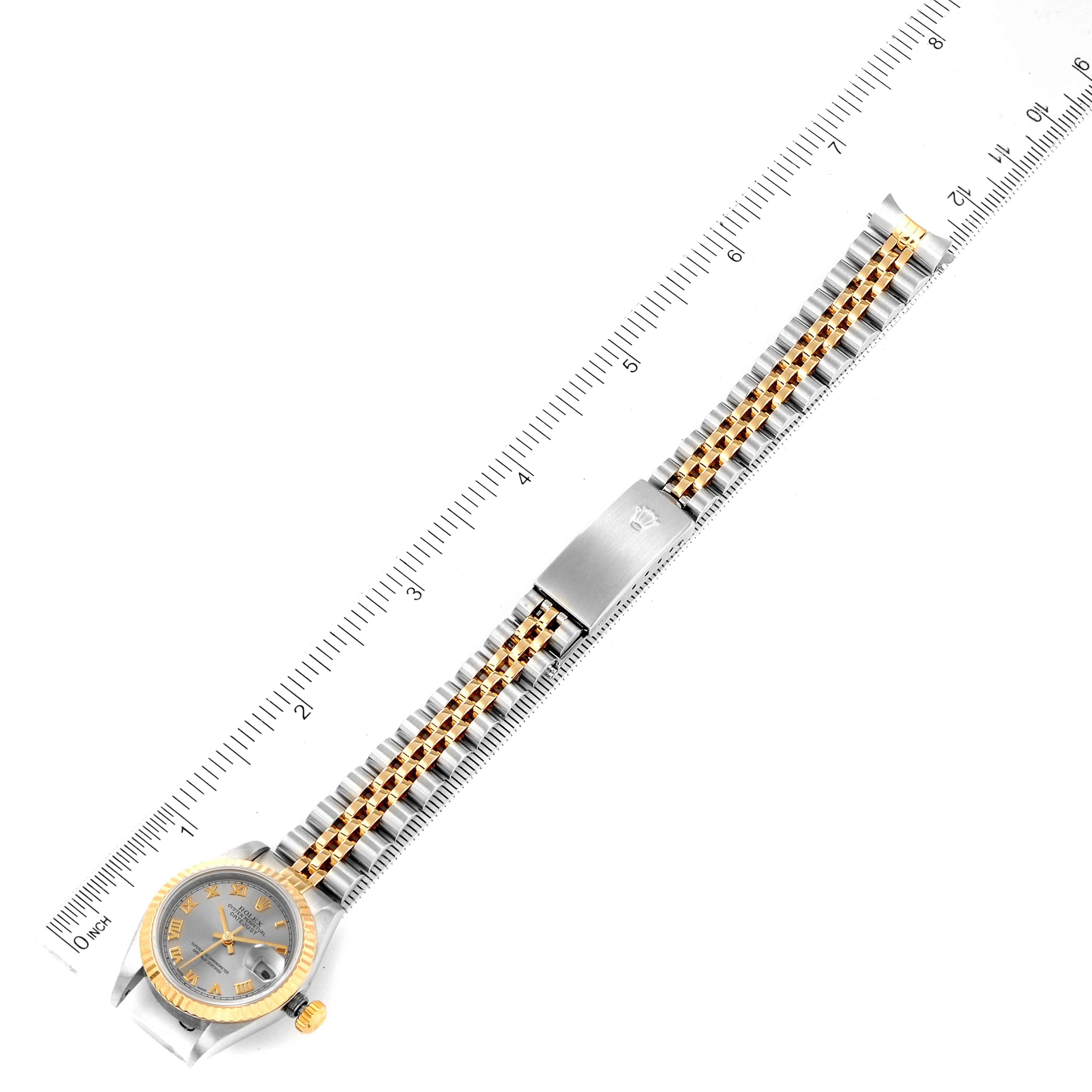 The image shows a Rolex Datejust 79173 Women
s Steel and Gold (two tone) Grey Dial 79173 Women
s Steel and Gold (two tone) Grey Dial watch laid flat with a ruler, highlighting its gold and silver bracelet and clasp.