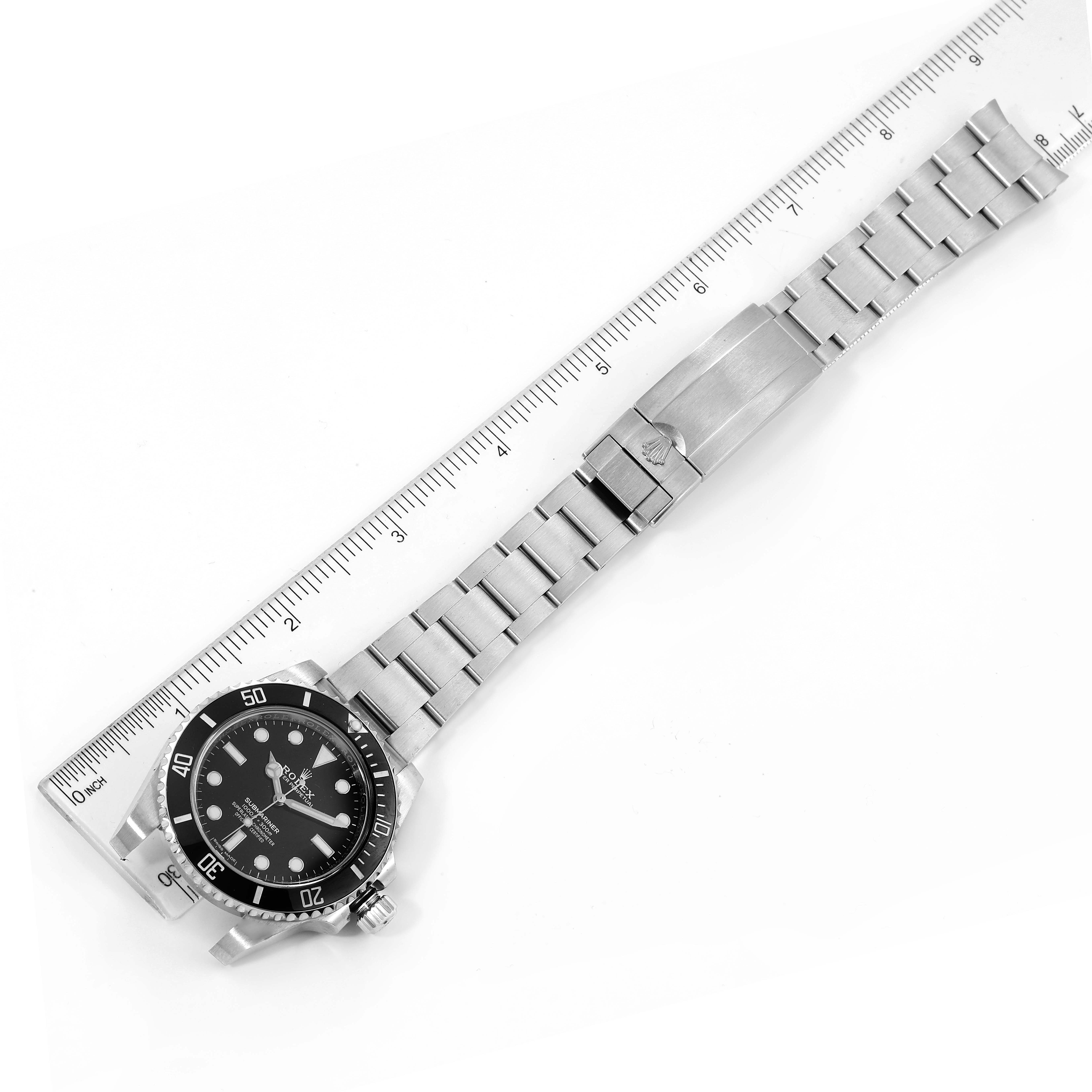 The Rolex Submariner 114060 Men
s Stainless Steel Black Dial 114060 Men
s Stainless Steel Black Dial watch is shown laid flat, displaying its face, bracelet, and clasp, alongside a ruler for scale.