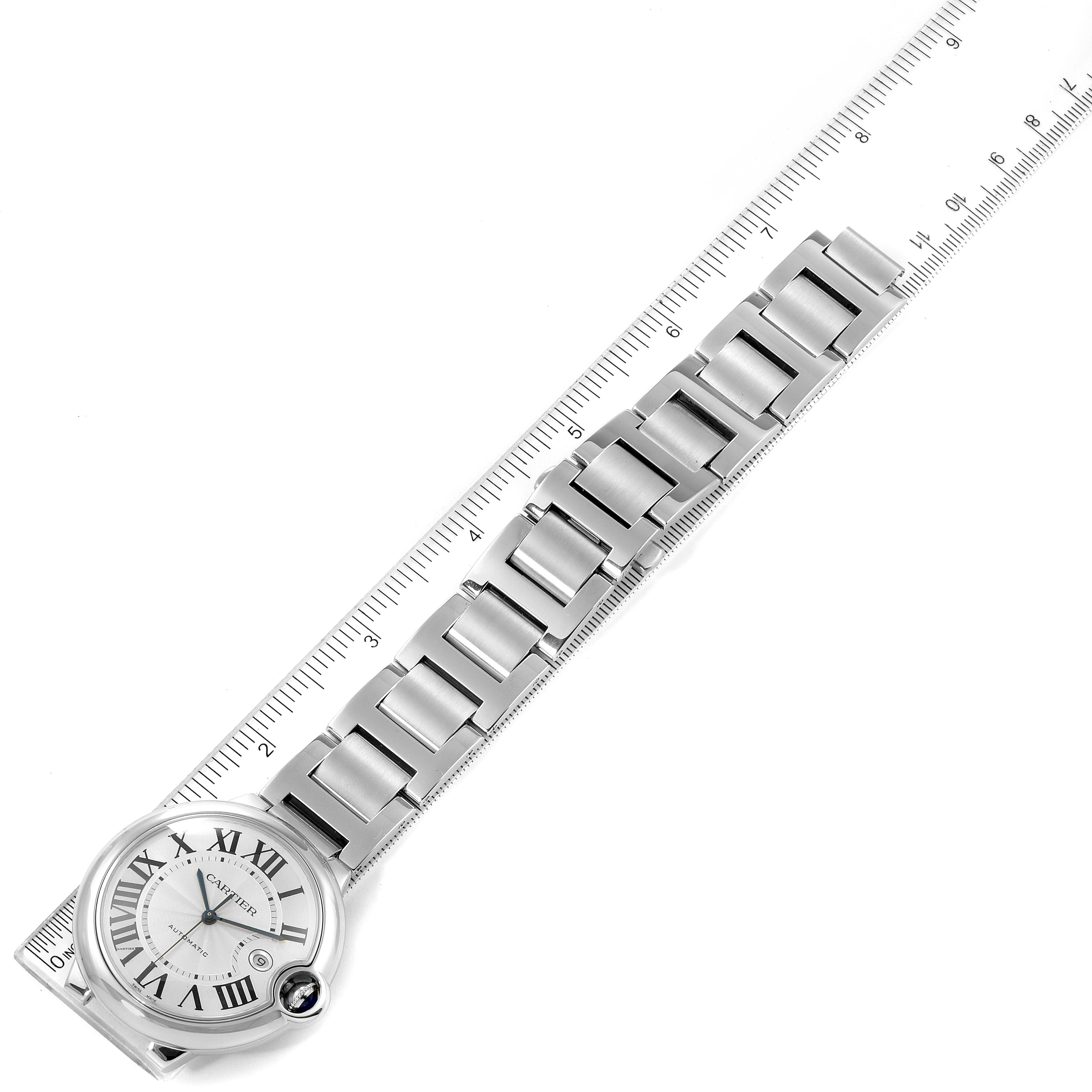 The image shows a top view of a Ballon Bleu model watch by Cartier, including the face and metal bracelet alongside a ruler.