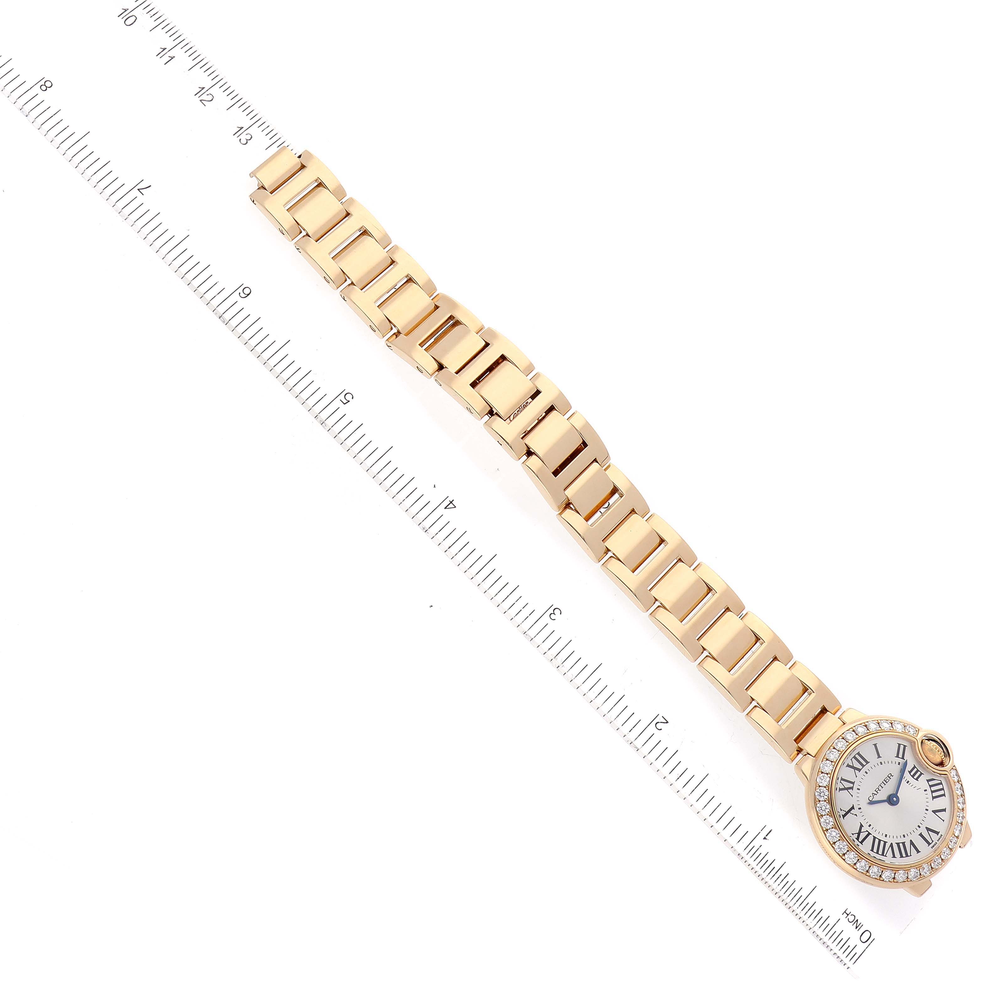 The image shows a Cartier Ballon Bleu WE9001Z3 Women's Yellow Gold Silver Dial WE9001Z3 Women's Yellow Gold Silver Dial watch laid flat next to a ruler, displaying the face and bracelet.