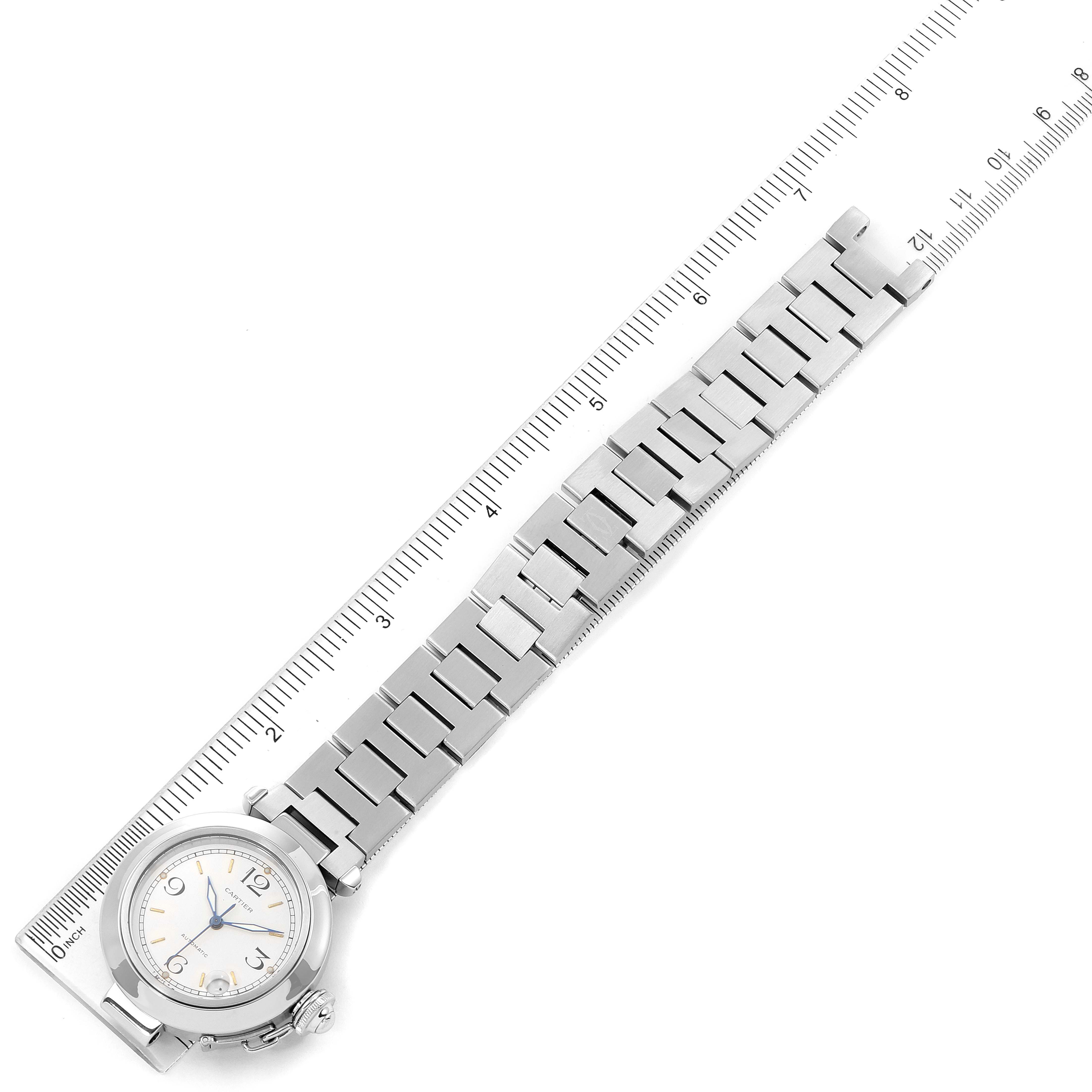 The image shows a top-down view of a Cartier Pasha W31044M7 Men's Stainless Steel White Dial W31044M7 Men's Stainless Steel White Dial watch, displaying its face, metal bracelet, and part of a ruler.