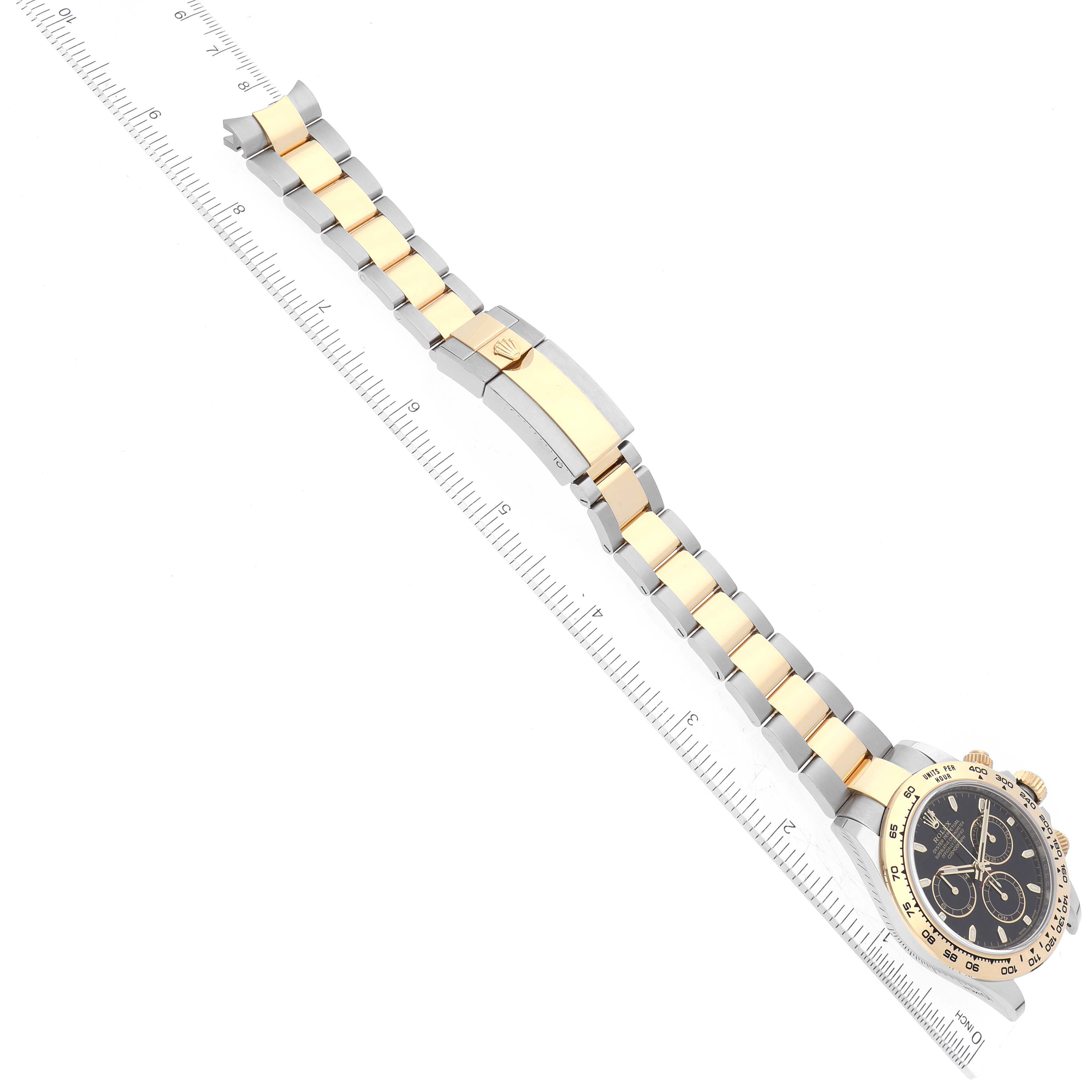 This image shows a top view of a Rolex Daytona 116503 Men
s Steel and Gold (two tone) Black Dial 116503 Men
s Steel and Gold (two tone) Black Dial watch with its bracelet and clasp extended alongside a ruler.