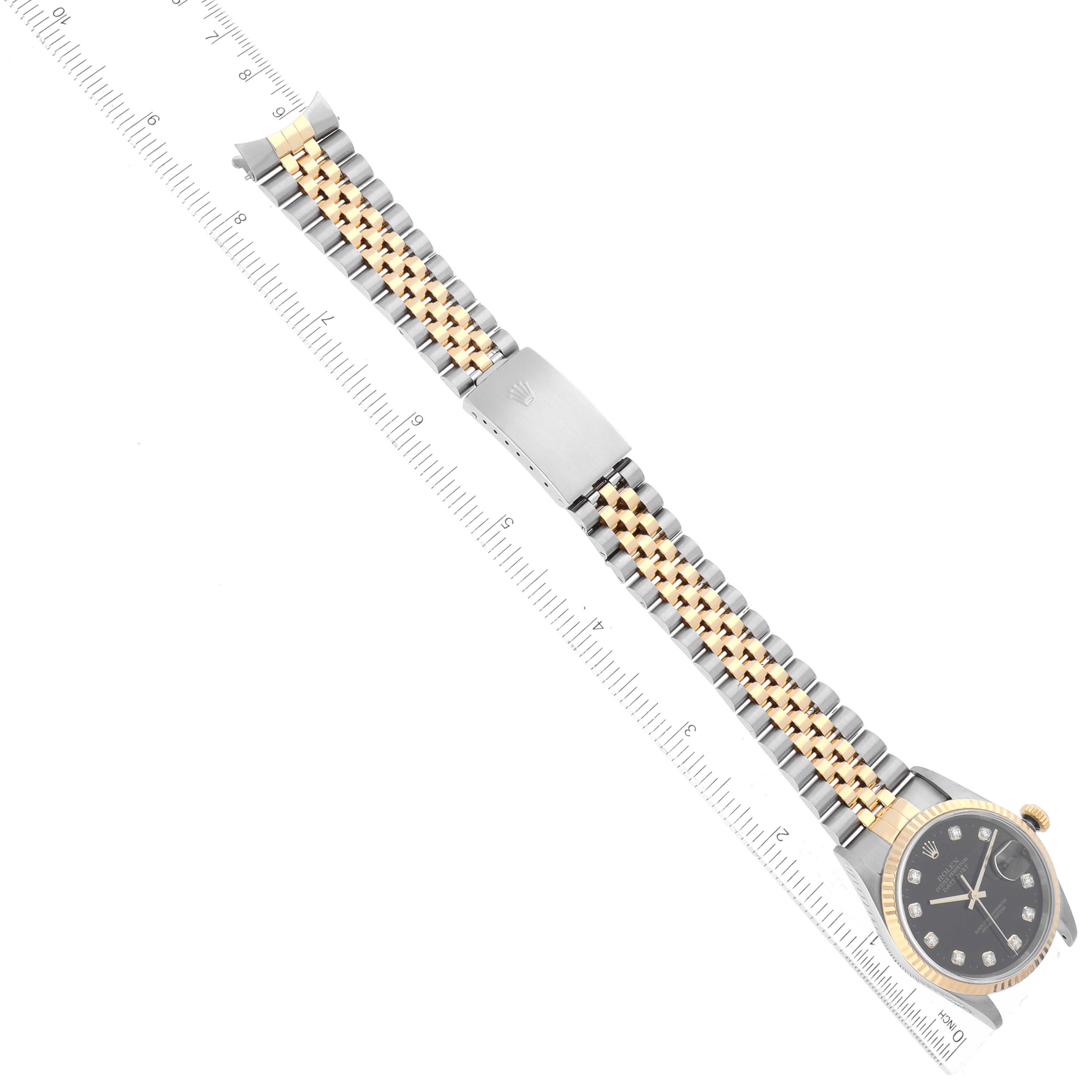 The Rolex Datejust 16233 Men's Steel and Gold (two tone) Black Dial 16233 Men's Steel and Gold (two tone) Black Dial watch is shown from above, highlighting its two-tone bracelet and clasp, accompanied by a ruler.