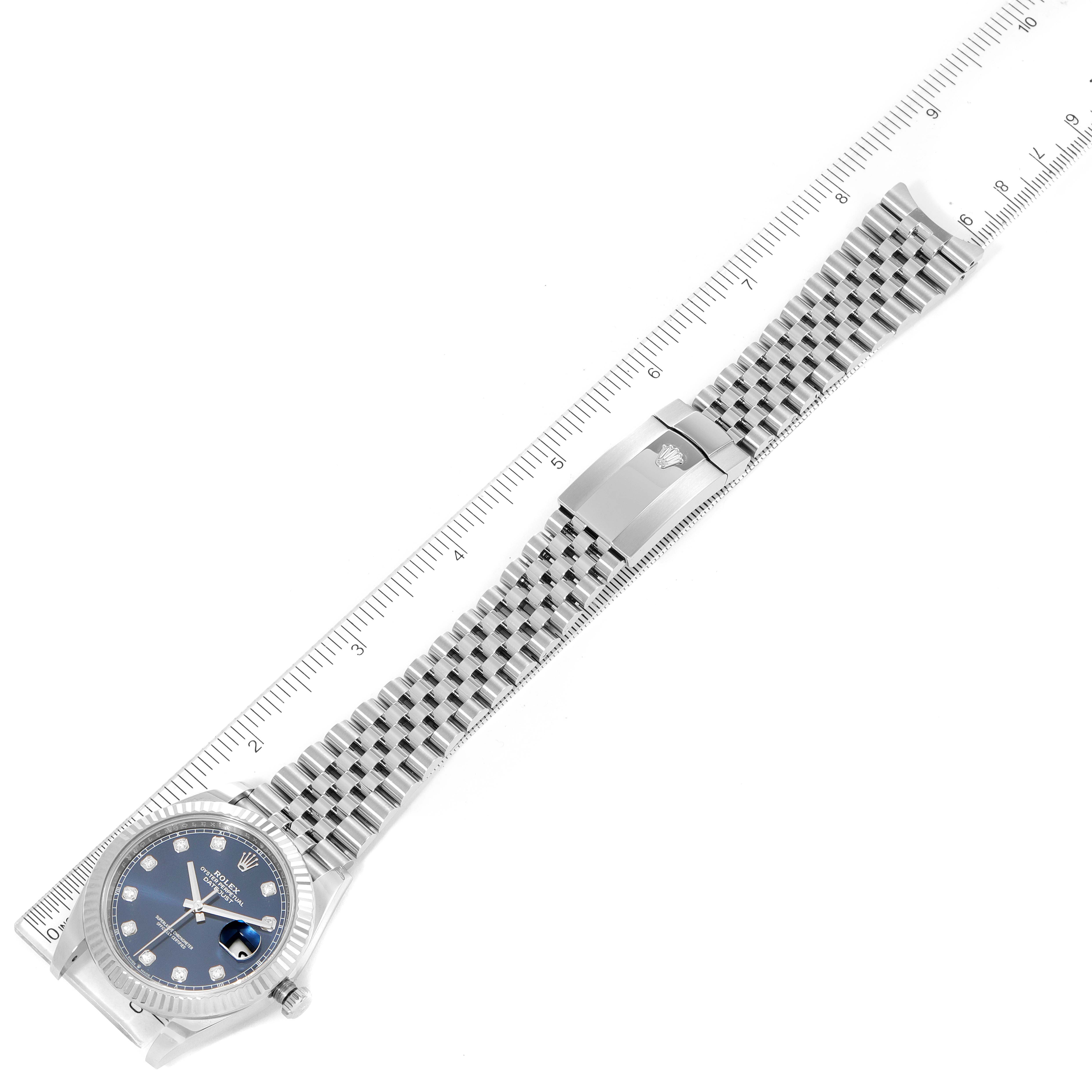 The Rolex Datejust 41 126334 Men's Stainless Steel Blue Dial 126334 Men's Stainless Steel Blue Dial watch is shown from an overhead angle, displaying the face, bezel, bracelet, and clasp alongside a measuring ruler.