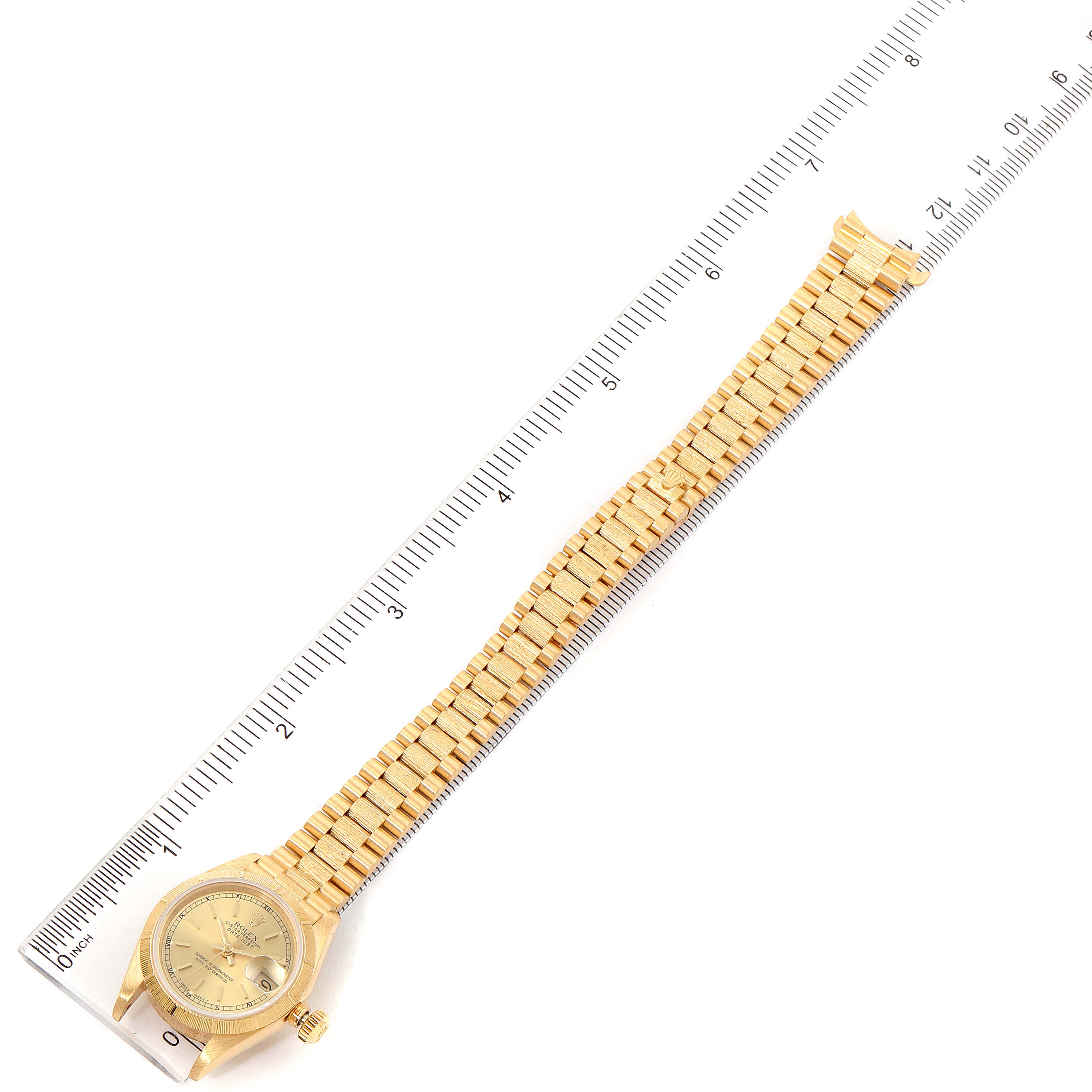 The image shows a Rolex President 69278 Women
s Yellow Gold Champagne Dial 69278 Women
s Yellow Gold Champagne Dial watch laid flat and measured by a ruler, displaying both the watch face and the bracelet.
