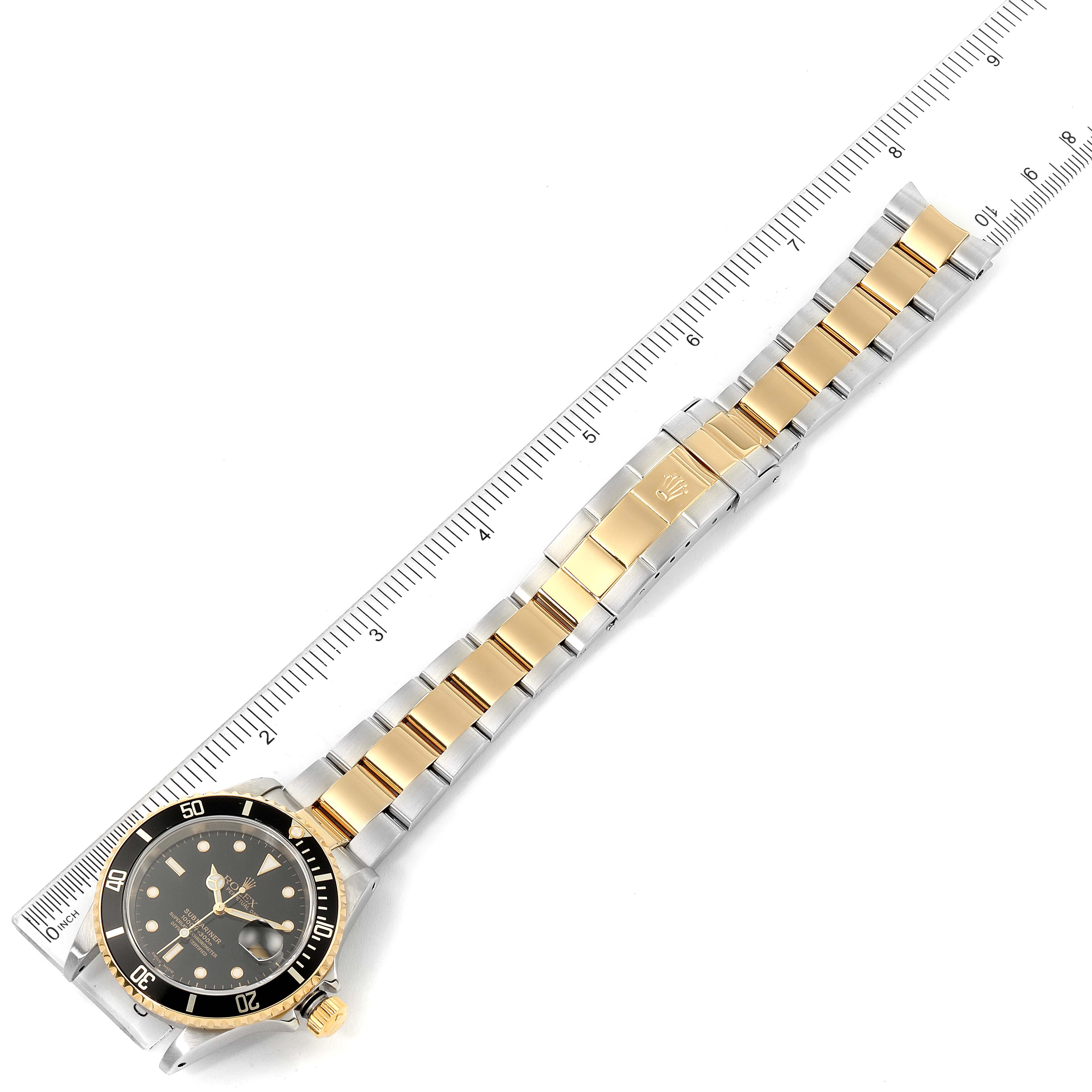 The image shows a top view of the Rolex Submariner 16613 Men's Steel and Gold (two tone) Black Dial 16613 Men's Steel and Gold (two tone) Black Dial watch, including its gold and silver bracelet next to a ruler for measurement.