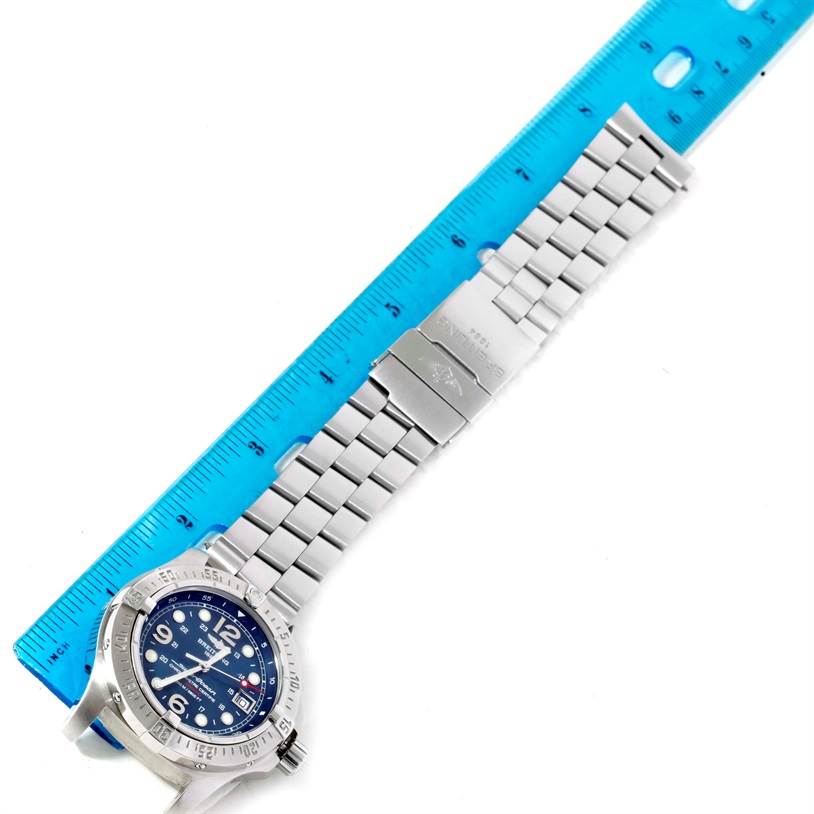 This image shows the Breitling Superocean A17390 Men's Stainless Steel Blue Dial A17390 Men's Stainless Steel Blue Dial watch fully extended next to a blue ruler, displaying its face and metal strap.