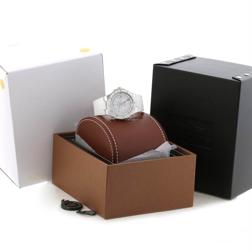 The Breitling Superocean A32380A9-A737 Stainless Steel White Dial A32380A9-A737 Stainless Steel White Dial watch is displayed at an angle showing its front, atop a brown cushion inside an open box, with additional packaging nearby.