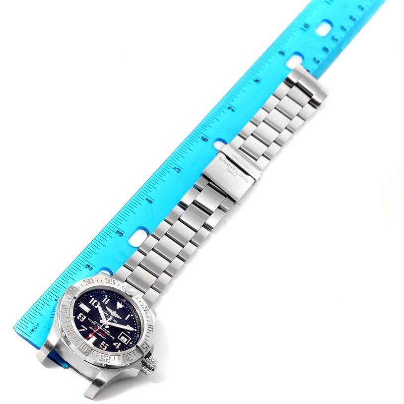 The image shows a Breitling Avenger A17331 Men's Stainless Steel Black Dial A17331 Men's Stainless Steel Black Dial watch laid flat next to a blue ruler, displaying its face and metal bracelet.