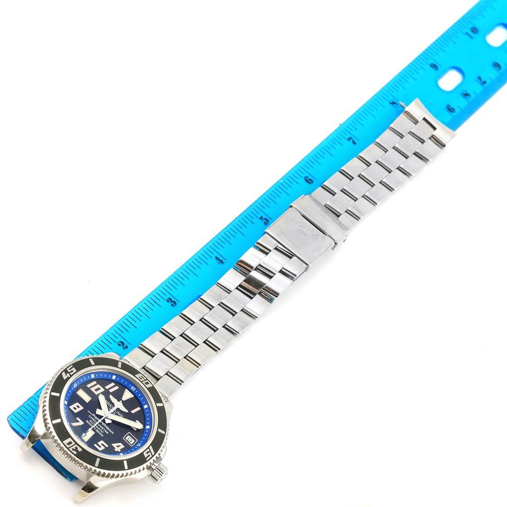 The image shows the Breitling Superocean A17364 Men's Stainless Steel Black Dial A17364 Men's Stainless Steel Black Dial watch laid flat with its stainless steel bracelet alongside a blue ruler.