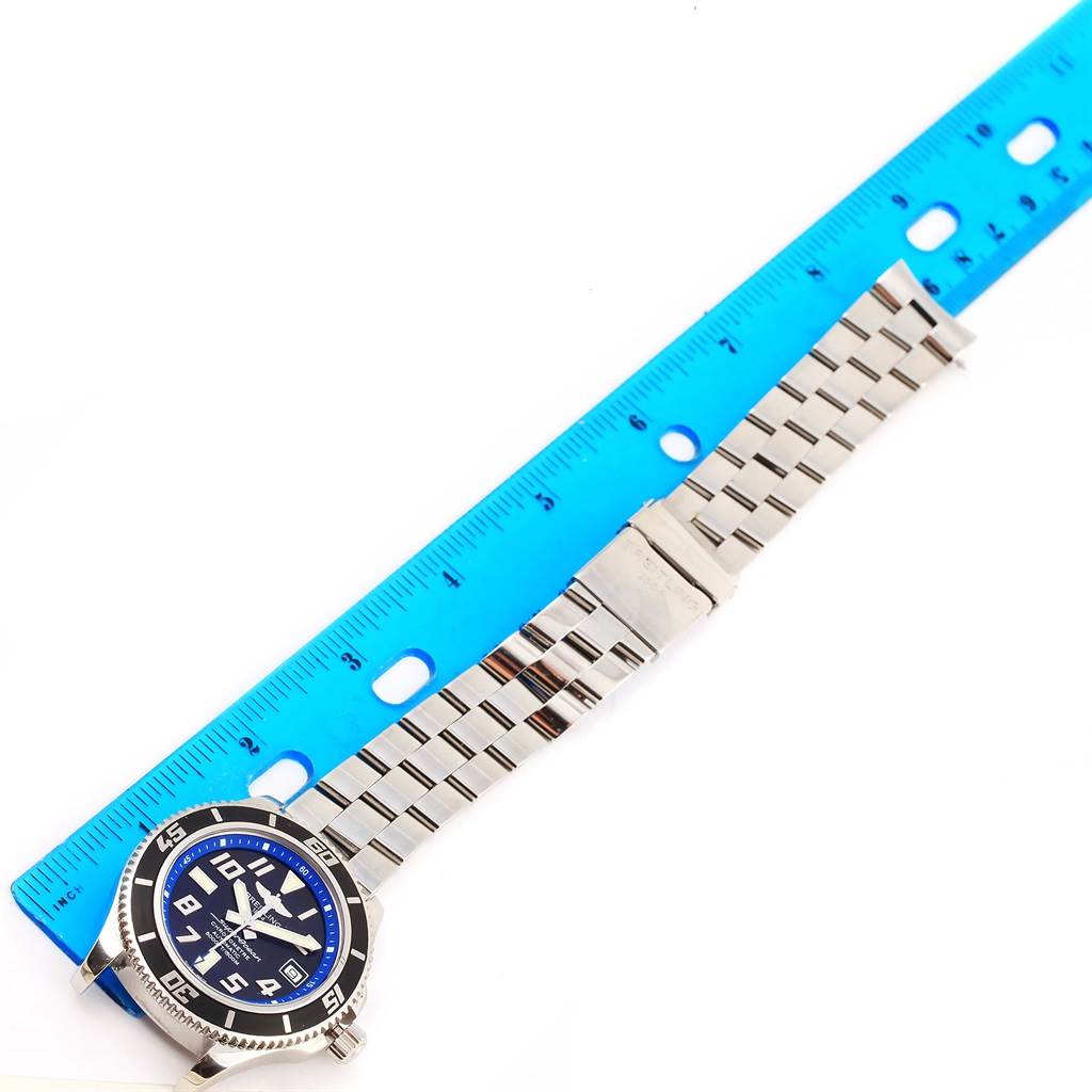 The image shows a top view of a Breitling Superocean A17364 Men's Stainless Steel Black Dial A17364 Men's Stainless Steel Black Dial watch with a blue dial and a metal bracelet next to a blue ruler.