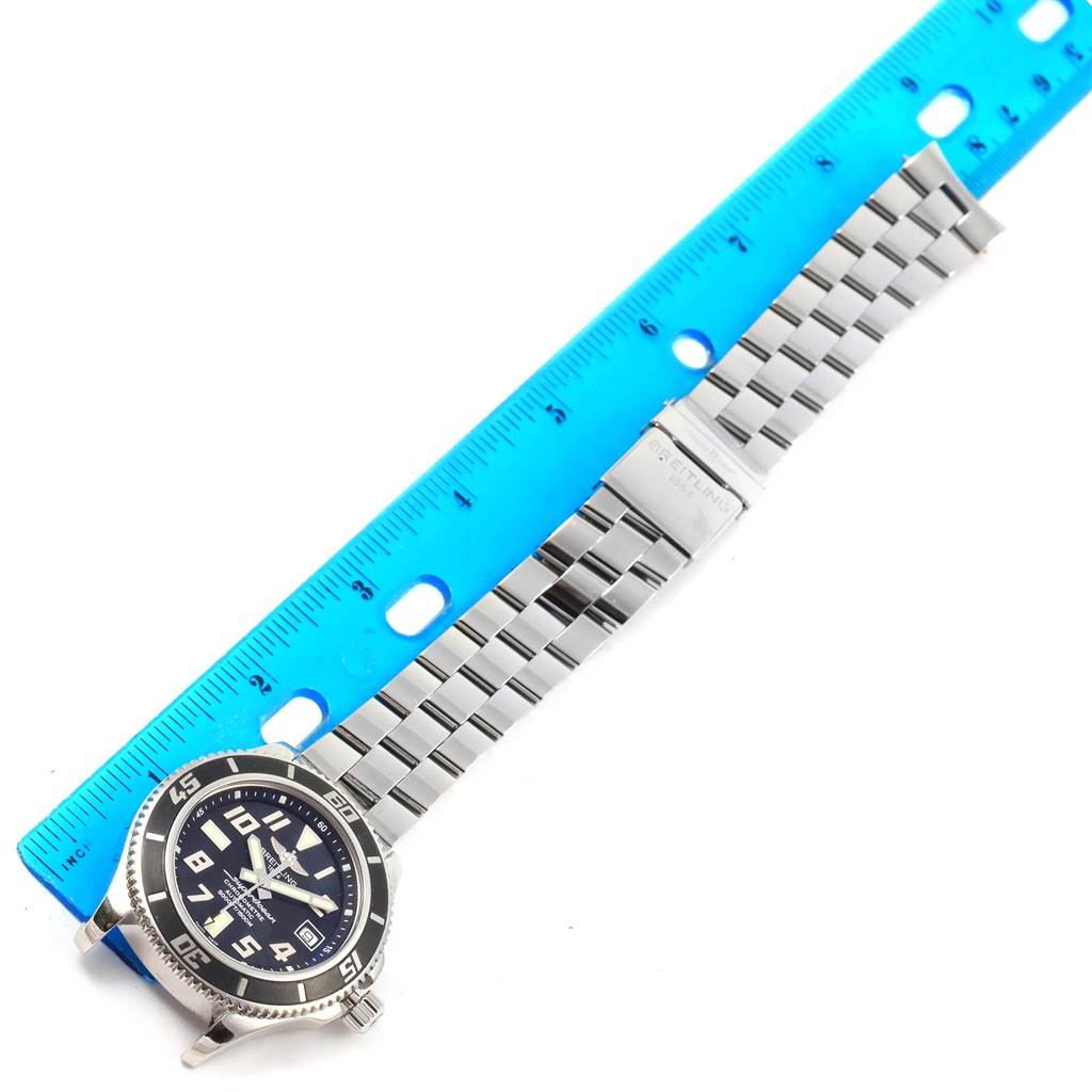 This image shows a top-down view of a Breitling Superocean A17364 Men's Stainless Steel Black Dial A17364 Men's Stainless Steel Black Dial watch with its metal bracelet laid out beside a blue ruler for scale.