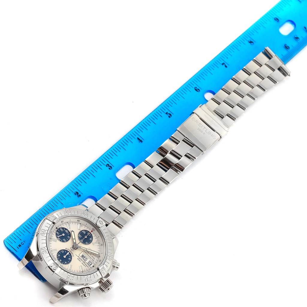 The image shows a top-down angle of a Breitling Superocean A13381 Men's Stainless Steel Beige Dial A13381 Men's Stainless Steel Beige Dial watch with its stainless steel bracelet beside a blue ruler for measurement.