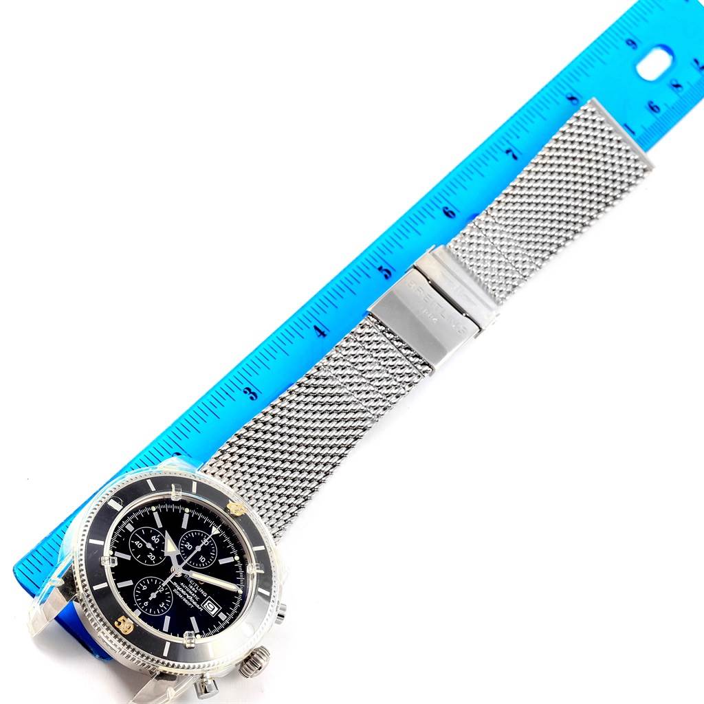 The image shows a Breitling Superocean A13320 Men's Stainless Steel Black Dial A13320 Men's Stainless Steel Black Dial watch from a top-down angle with a metal mesh bracelet and a blue measuring ruler for scale.