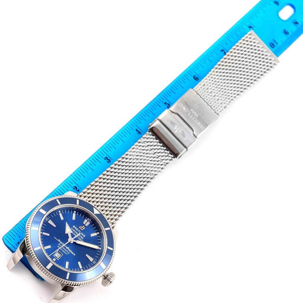 The image shows a top-down view of a Breitling Superocean A17320 Men's Stainless Steel Blue Dial A17320 Men's Stainless Steel Blue Dial watch with a blue dial and mesh bracelet, placed next to a blue ruler.