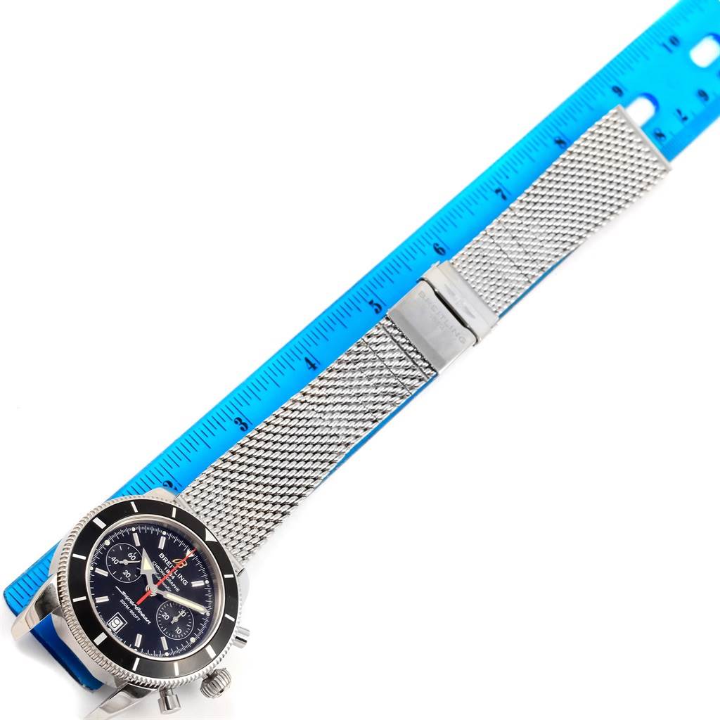 The image shows a top-down view of a Breitling Superocean A23370 Men's Stainless Steel Black Dial A23370 Men's Stainless Steel Black Dial watch with a metal mesh strap next to a ruler.