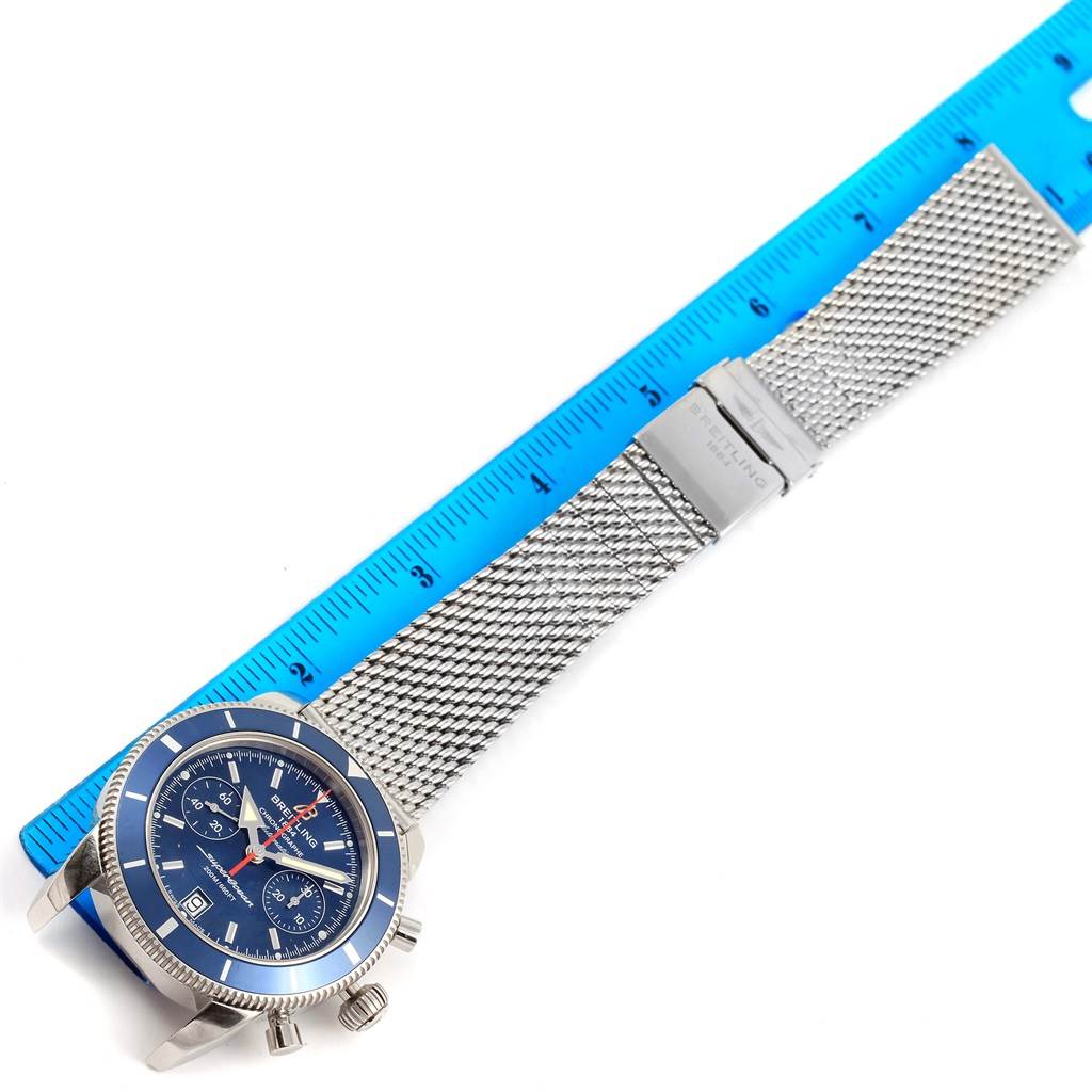The image shows a Breitling Superocean A23370 Men's Stainless Steel Blue Dial A23370 Men's Stainless Steel Blue Dial watch, including its face, bezel, crown, and mesh bracelet, next to a blue ruler for scale.