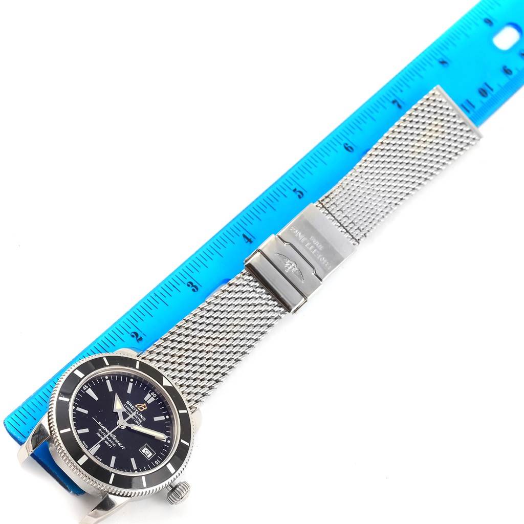 This image shows a Breitling Superocean A17321 Men's Stainless Steel Black Dial A17321 Men's Stainless Steel Black Dial watch lying flat with its mesh strap and clasp fully visible, alongside a blue ruler for scale.
