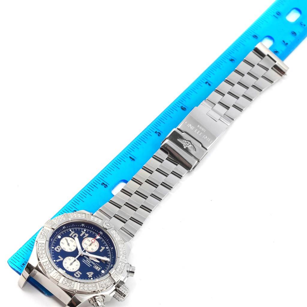 The image shows a top-down view of a Breitling Avenger A13370 Men's Stainless Steel Blue Dial A13370 Men's Stainless Steel Blue Dial watch with a stainless steel bracelet next to a blue ruler.