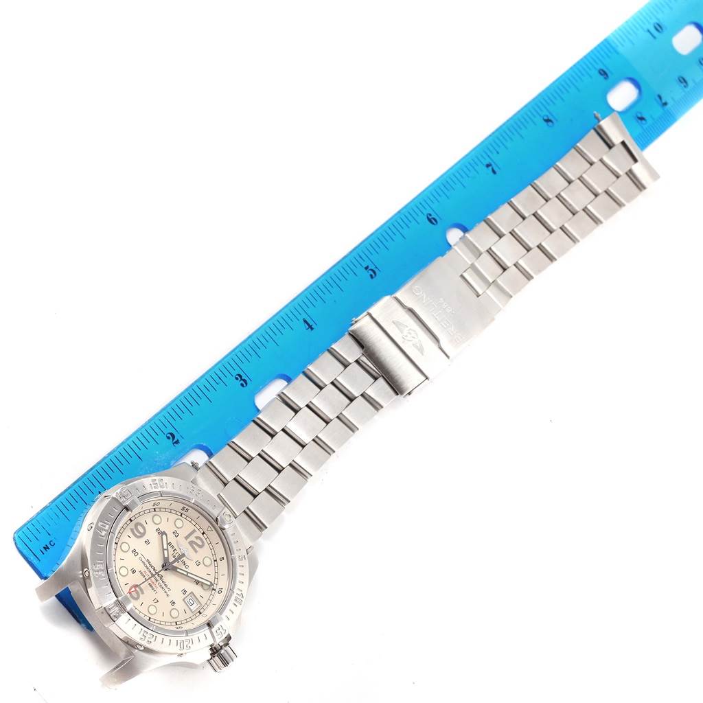 The image shows a top-down view of a Breitling Superocean A17390 Men's Stainless Steel Silver Dial A17390 Men's Stainless Steel Silver Dial watch with a metal strap, placed next to a blue ruler for scale.