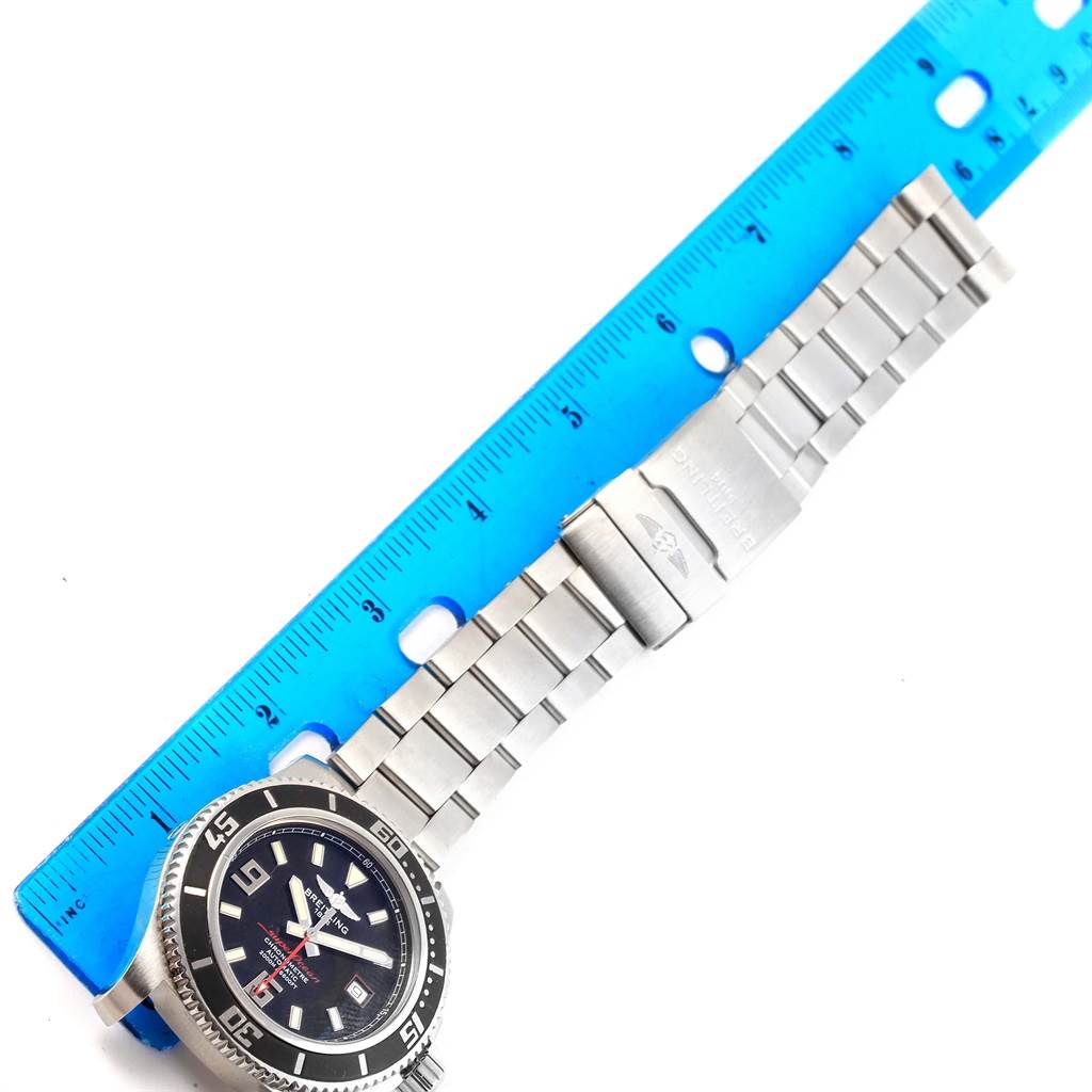 The image shows a top-down view of a Breitling Superocean A17391 Men's Stainless Steel Black Dial A17391 Men's Stainless Steel Black Dial watch with a stainless steel bracelet next to a blue measuring ruler.
