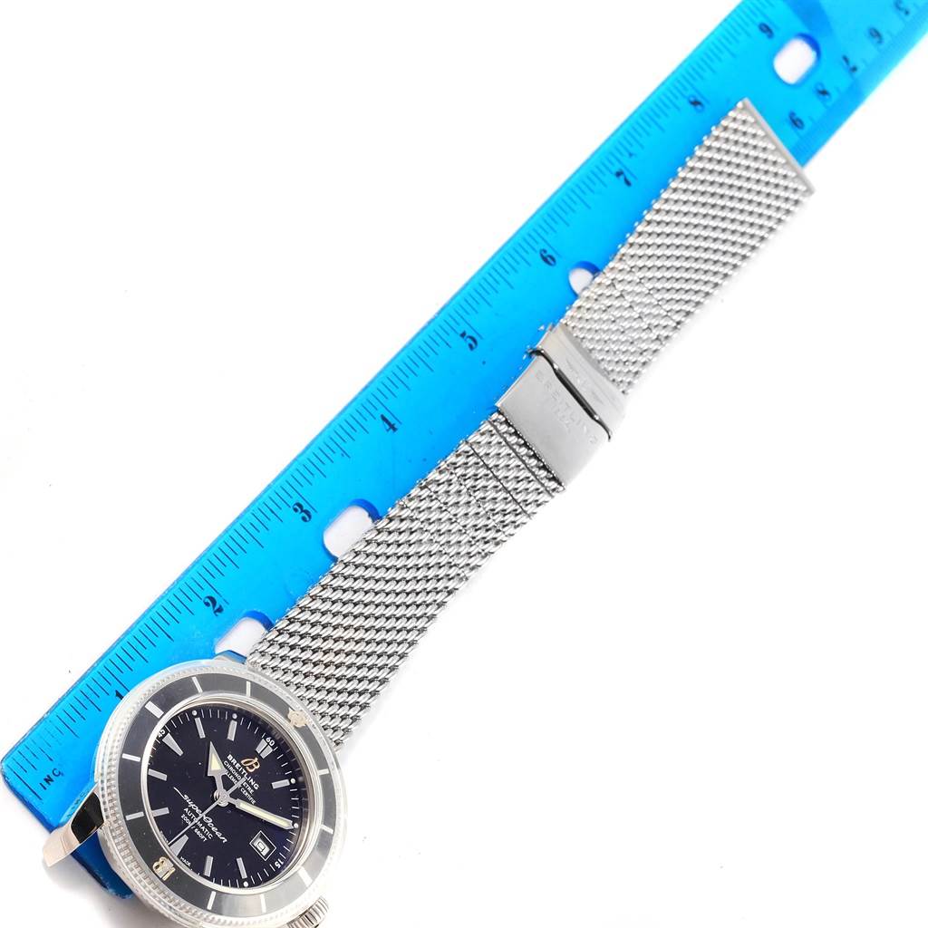 This image shows a Breitling Superocean A17321 Men's Stainless Steel Black Dial A17321 Men's Stainless Steel Black Dial watch with its face and mesh strap, measured against a blue ruler.