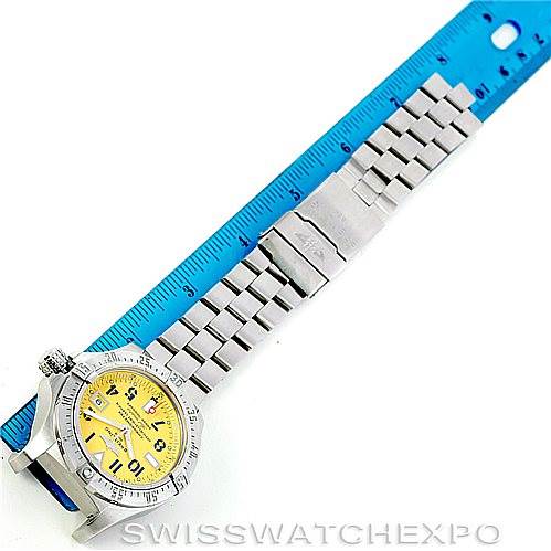 The image shows a top-down view of a Breitling Avenger A17330 Men's Stainless Steel Yellow Dial A17330 Men's Stainless Steel Yellow Dial watch with a yellow dial, measuring its metal band against a blue ruler.