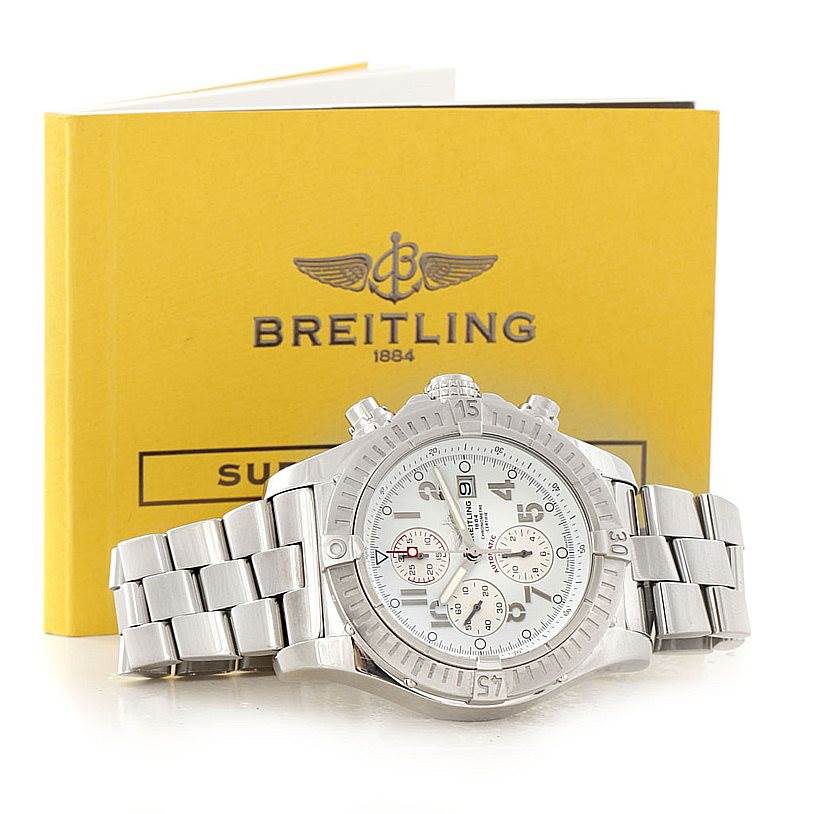 This image shows a Breitling Avenger A13370 Men's Stainless Steel White Dial A13370 Men's Stainless Steel White Dial watch and its metal bracelet from a front angle, with its manual in the background.