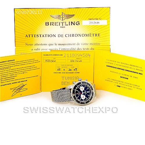 The image shows a Breitling Superocean A23320 Men's Stainless Steel Black Dial A23320 Men's Stainless Steel Black Dial watch with its mesh bracelet, placed in front of its yellow Certificates of Chronometer.