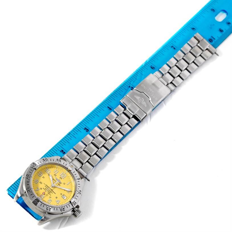 The Breitling Superocean A17345 Men's Stainless Steel Yellow Dial A17345 Men's Stainless Steel Yellow Dial watch is shown flat, displaying its yellow dial, stainless steel bezel, and bracelet laid next to a blue ruler.
