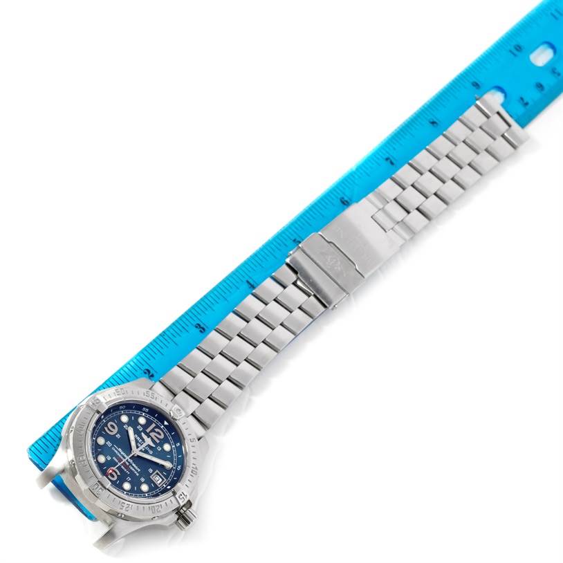 The Breitling Superocean A17390 Men's Stainless Steel Blue Dial A17390 Men's Stainless Steel Blue Dial watch is shown from an overhead angle, displaying its entire face and metal bracelet alongside a blue ruler.