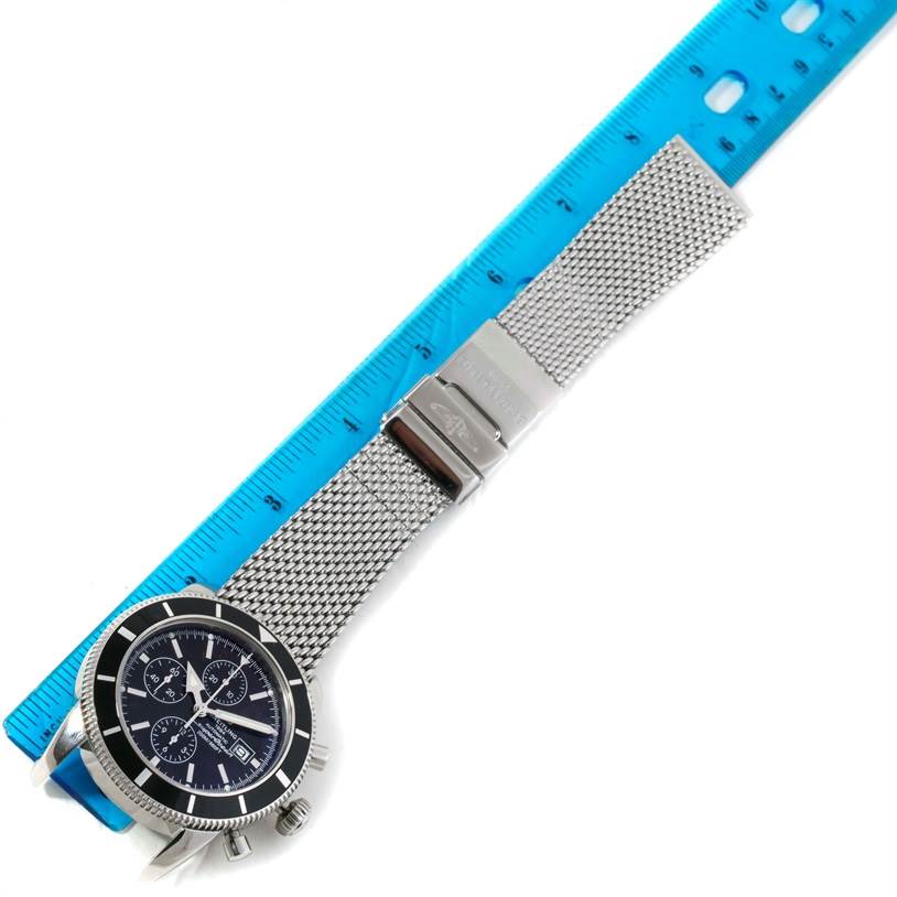 The Breitling Superocean A13320 Men's Stainless Steel Black Dial A13320 Men's Stainless Steel Black Dial watch is shown from an angled top view, featuring its face, bezel, and metal mesh bracelet alongside a blue ruler.