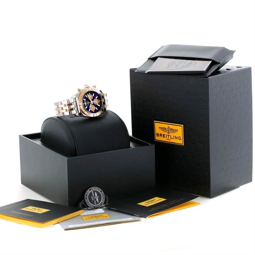 The image shows a Breitling Chronomat CB0110 Men's Steel and Gold (two tone) Black Dial CB0110 Men's Steel and Gold (two tone) Black Dial watch at a slight angle, accompanied by its box, manuals, and accessories.