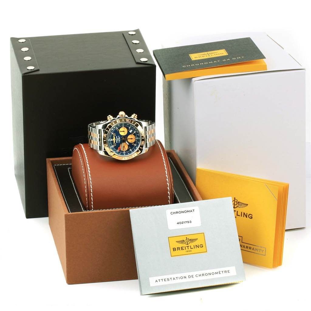 The Breitling Chronomat CB042012/C858 Men's Steel and Gold (two tone) Blue Dial CB042012/C858 Men's Steel and Gold (two tone) Blue Dial watch is displayed at an angle showing its face and bracelet, with its box and documentation in the background.