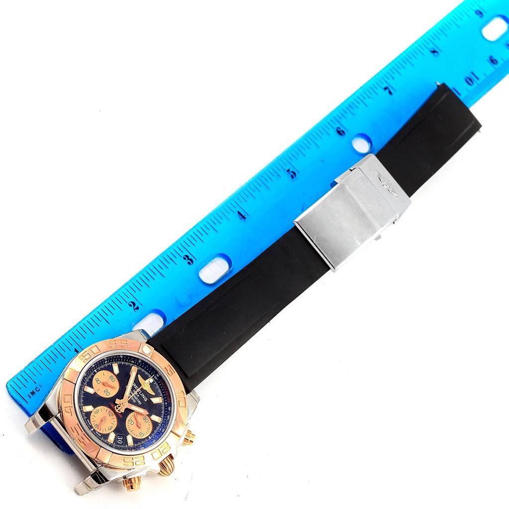 This image shows a top-view angle of a Breitling Chronomat CB0140 Men's Steel and Gold (two tone) Black Dial CB0140 Men's Steel and Gold (two tone) Black Dial watch with a black strap and a blue measuring ruler for scale.