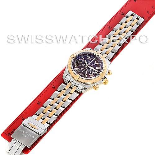 The image shows a top-down view of a Breitling Chronomat C1335611/K515-TT Men
s Stainless Steel Burgundy Dial C1335611/K515-TT Men
s Stainless Steel Burgundy Dial watch with a metal bracelet laid on a red ruler.