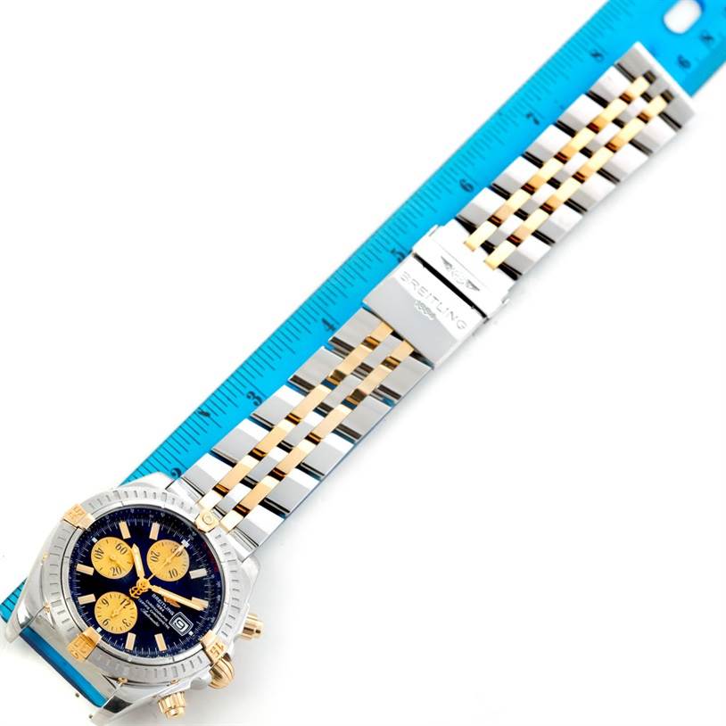 The image shows a top-down view of a Breitling Chronomat B13356 Men's Steel and Gold (two tone) Black Dial B13356 Men's Steel and Gold (two tone) Black Dial watch aligned with a ruler, highlighting the watch face and metal bracelet.