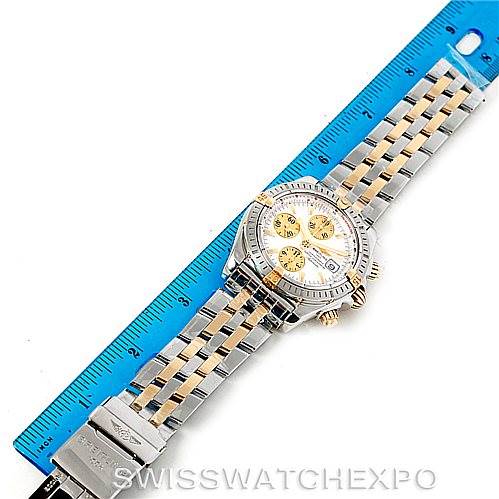 The image shows a Breitling Chronomat B13356 Men's Steel and Gold (two tone) Silver Dial B13356 Men's Steel and Gold (two tone) Silver Dial watch laid flat next to a blue ruler, highlighting its bracelet and case.
