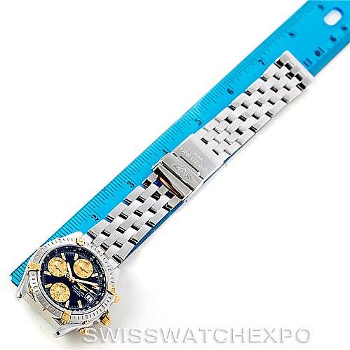 This image shows a top-down view of the Breitling Chronomat B13352 Men
s Steel and Gold (two tone) Black Dial B13352 Men
s Steel and Gold (two tone) Black Dial watch, including its bracelet and clasp, next to a ruler.